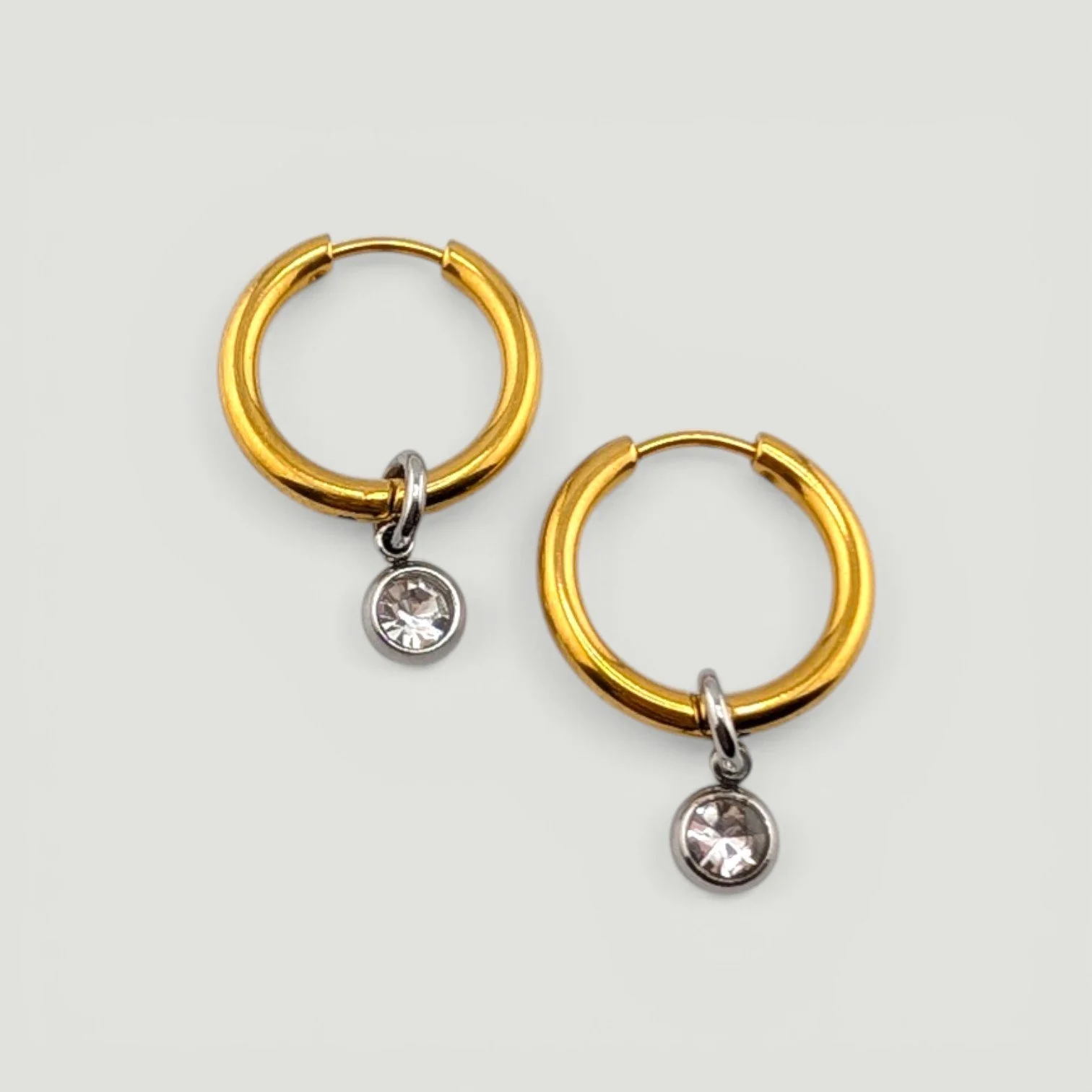 Gold huggie hoop earrings with silver bezel-set rhinestone charms, two-tone flat lay