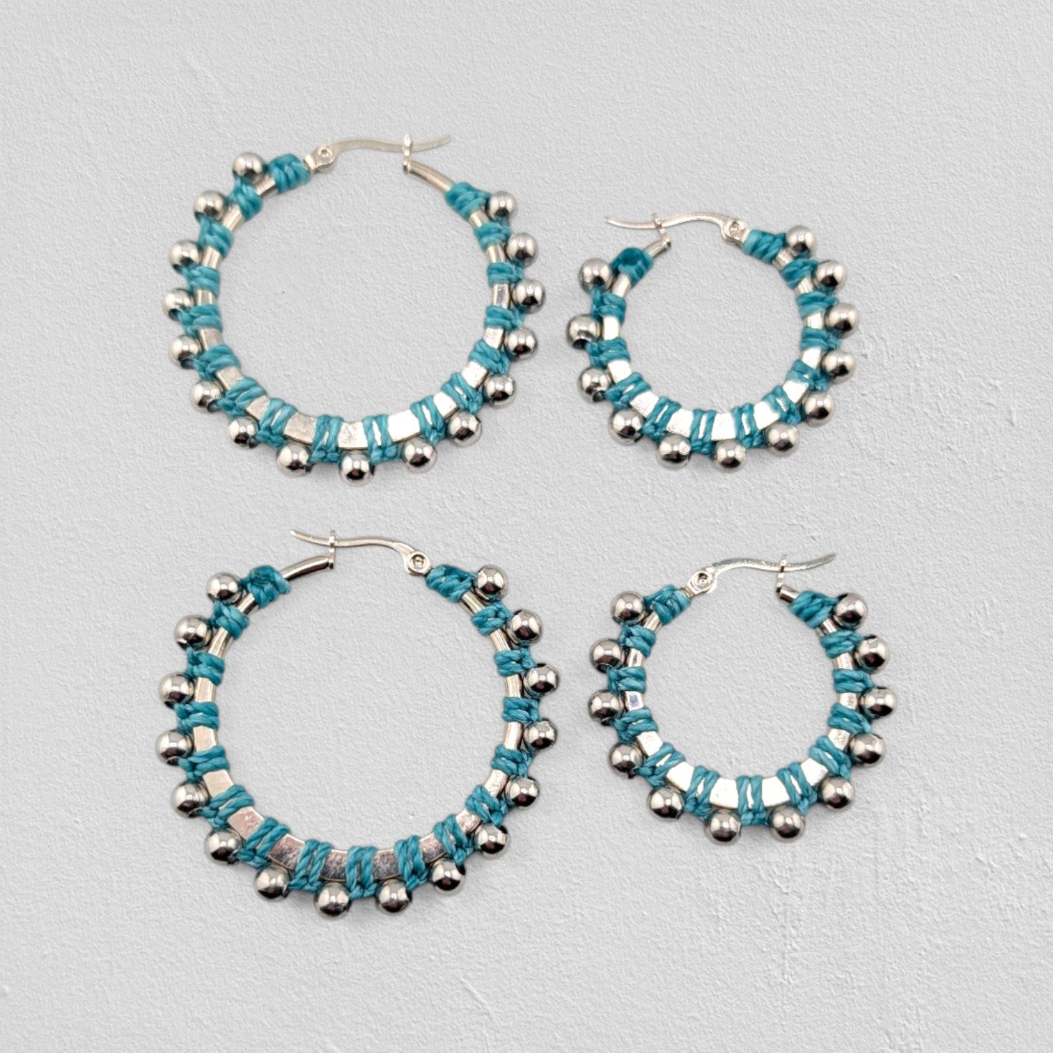 Turquoise beaded macramé stainless steel hoop earrings in silver, 30 mm and 40 mm sizes side by side, flat lay on a neutral background