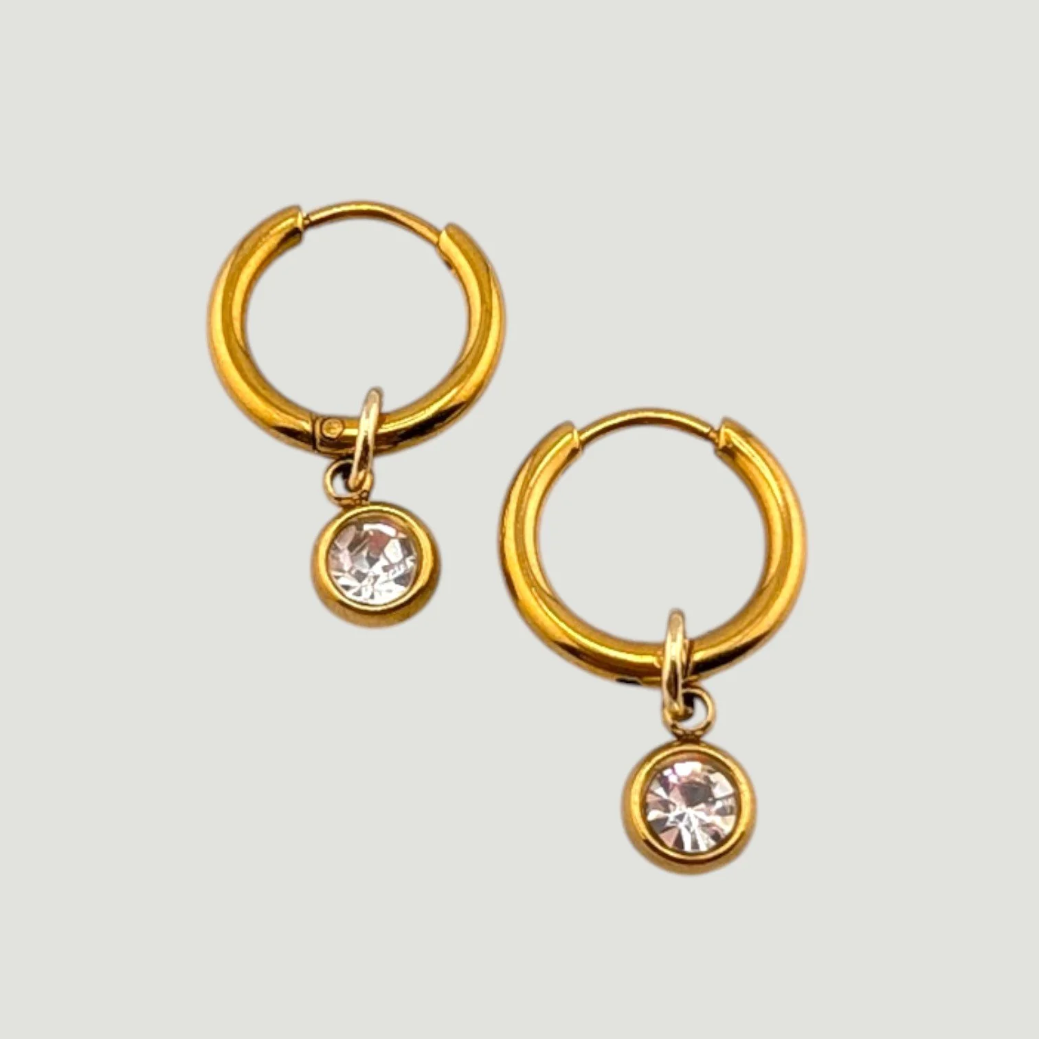Gold evil eye stainless steel huggie hoop earrings with rhinestone and medallion charms flat lay