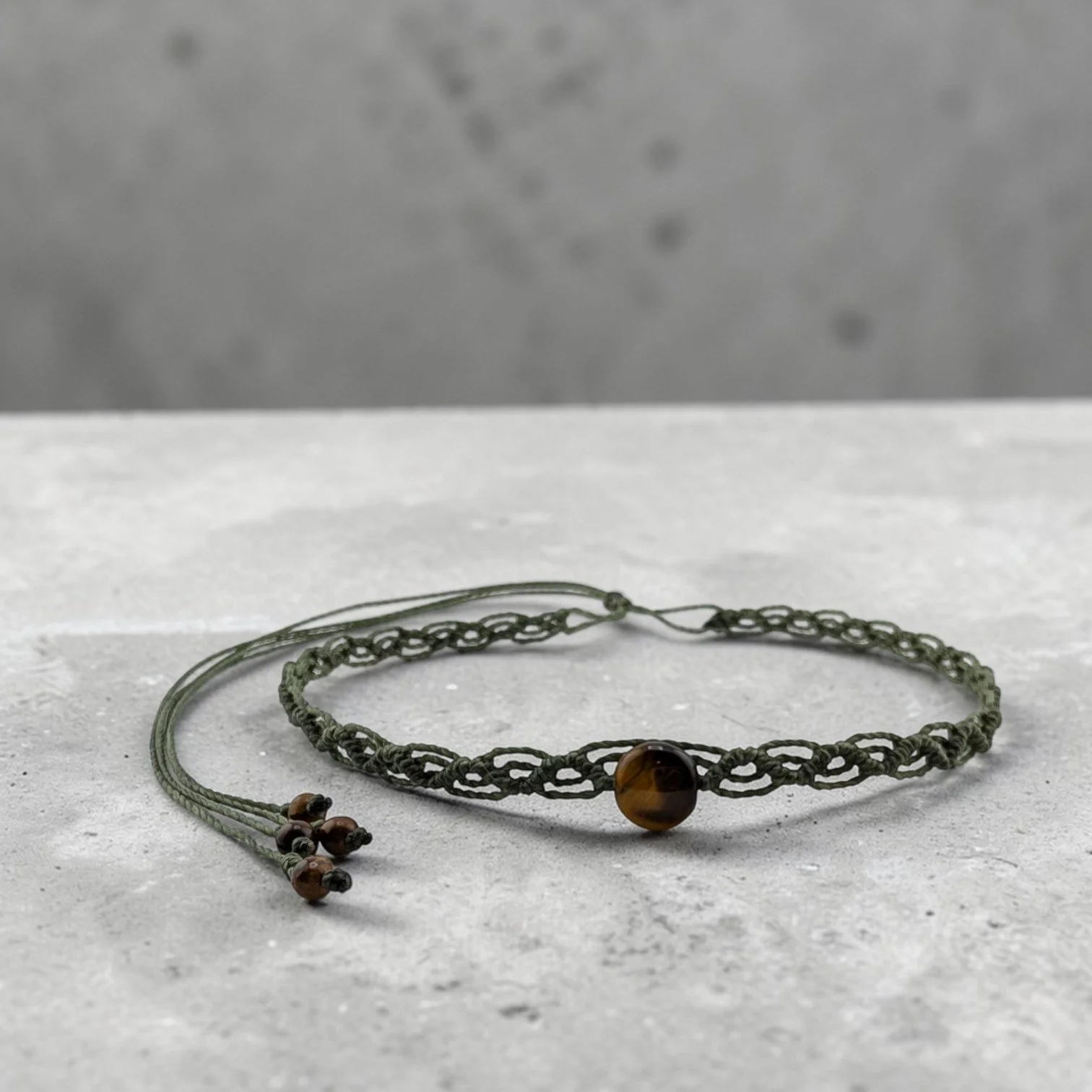 Western macrame woven choker with a tiger eye centerpiece displayed on a textured ciment shelf