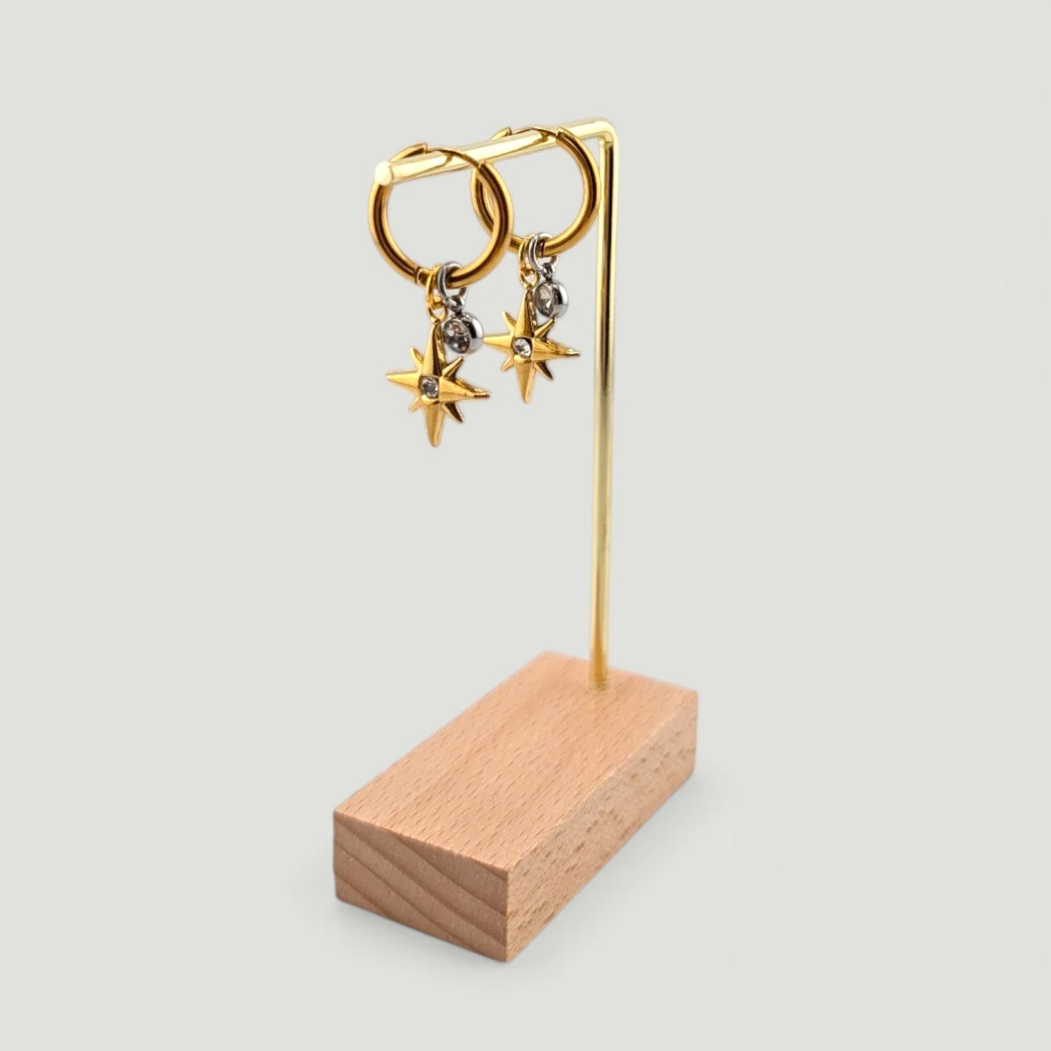 Northern star huggie hoop earrings with rhinestone charms on an earring stand, showing full drop and layered design