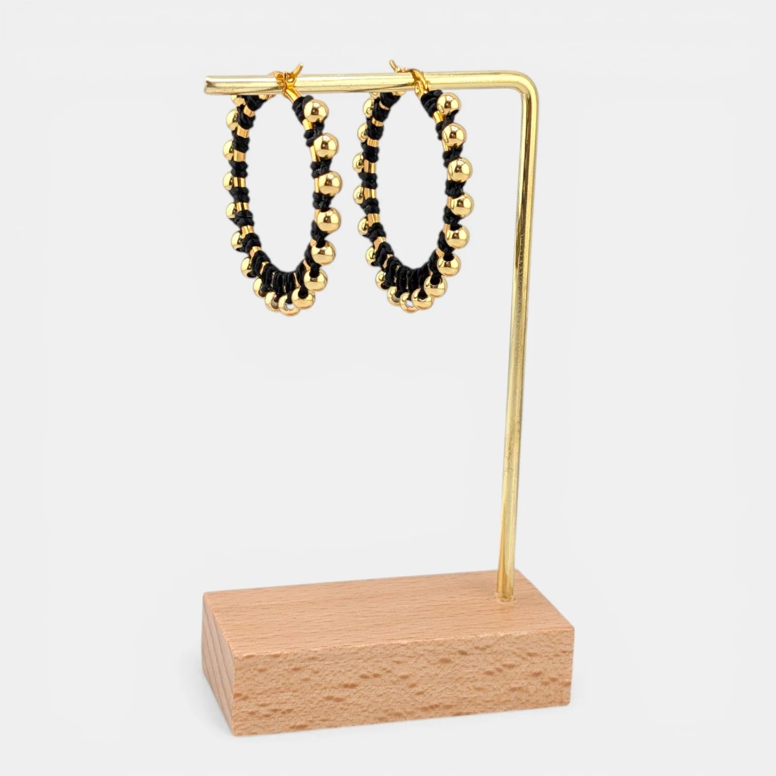 black beaded macramé stainless steel hoop earrings in gold, 40 mm drop shown on earring display stand
