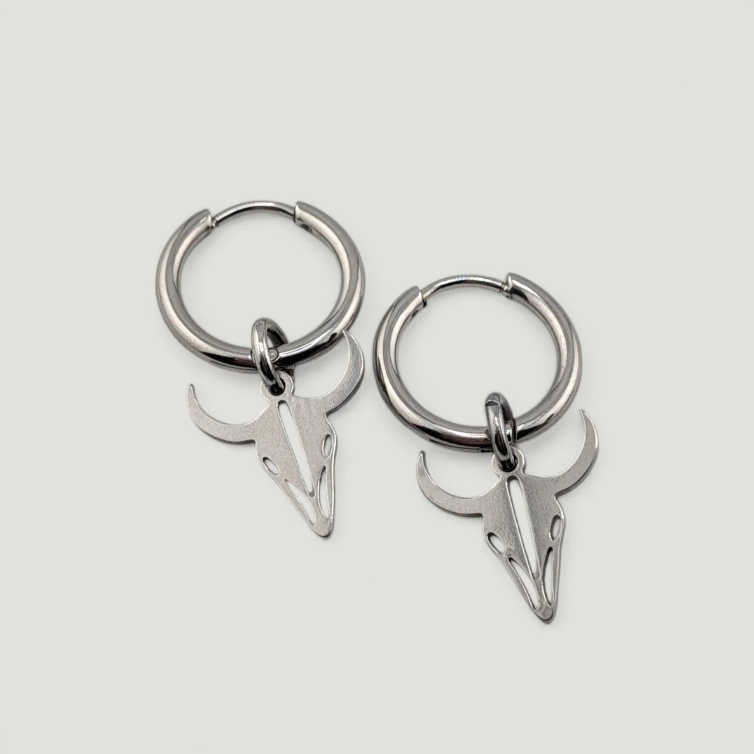 Bull skull stainless steel huggie hoop earrings in silver, flat lay