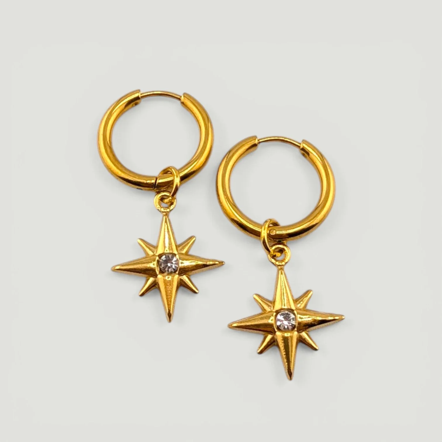 Gold huggie hoop earrings with northern star charms, celestial design flat lay