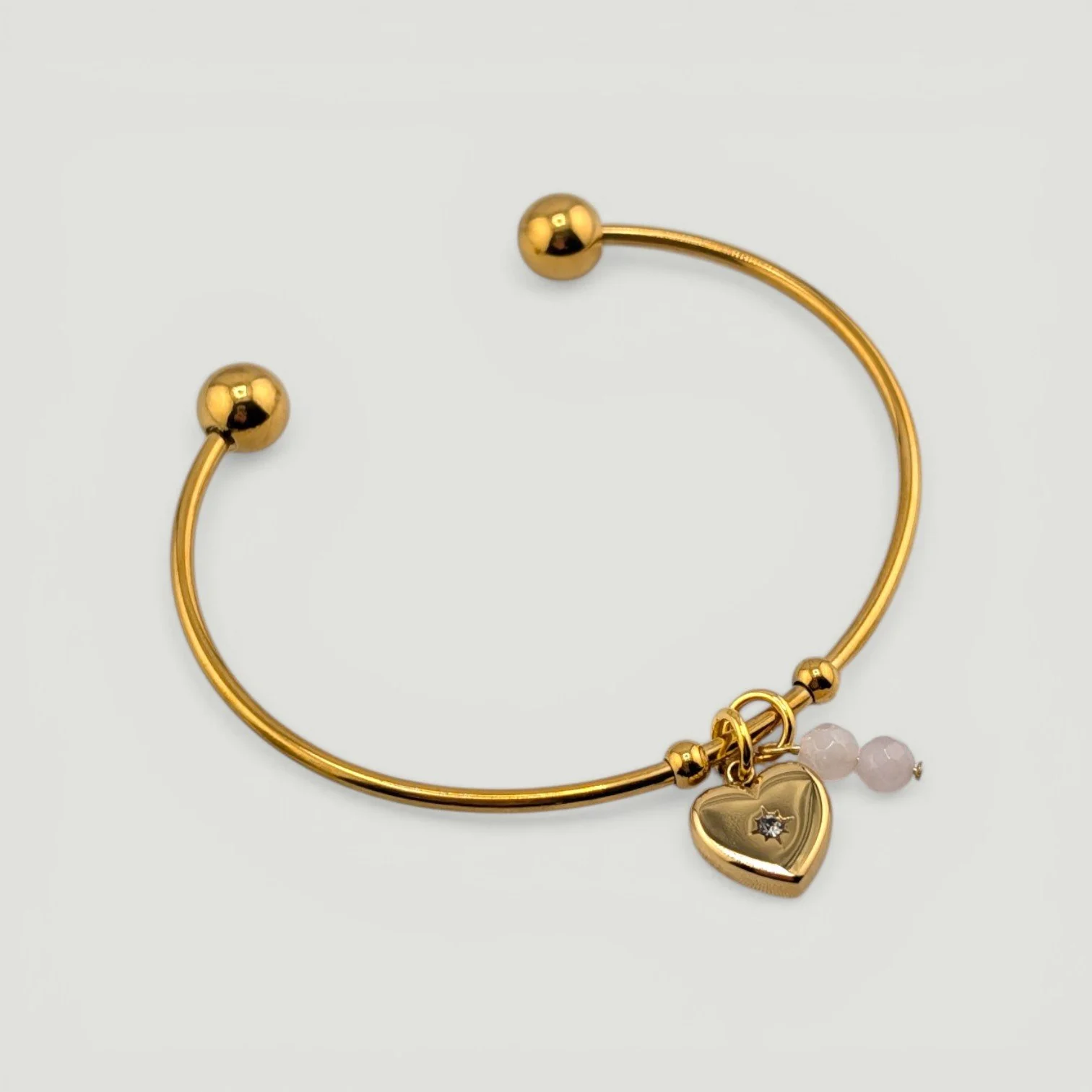 Gold starburst heart stainless steel bangle bracelet with rose quartz charm, full flat lay