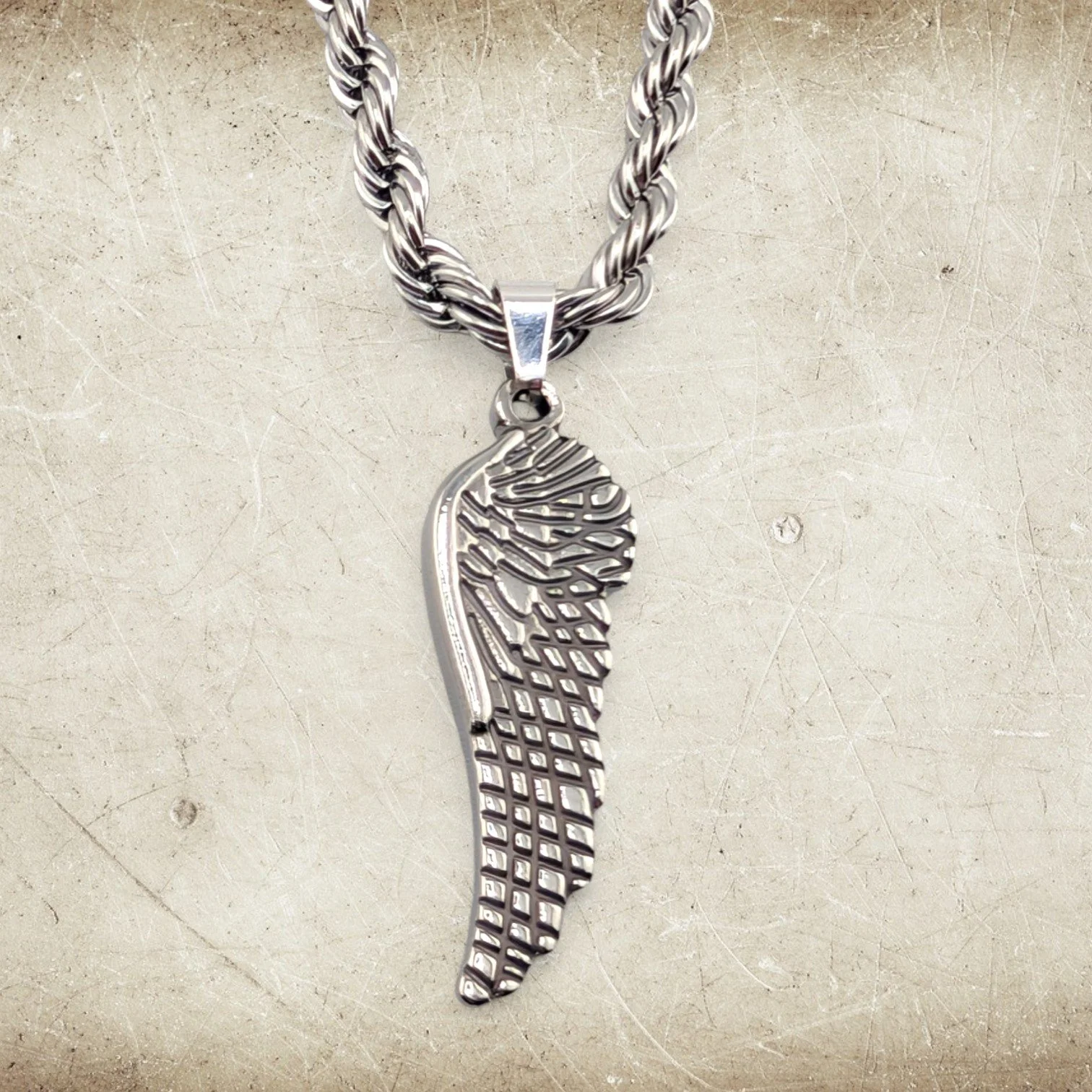 men's wing stainless steel necklace front view close-up showing sculpted wing pendant detail on textured background