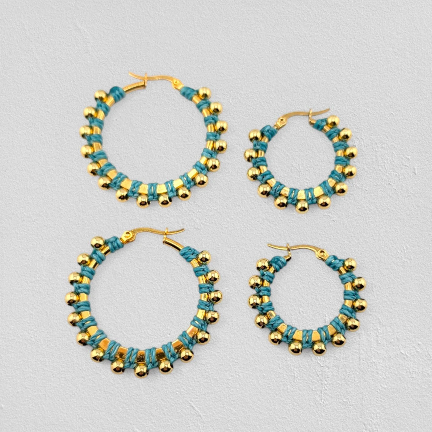 Turquoise beaded macramé stainless steel hoop earrings in gold, 30 mm and 40 mm sizes side by side, flat lay on a neutral background
