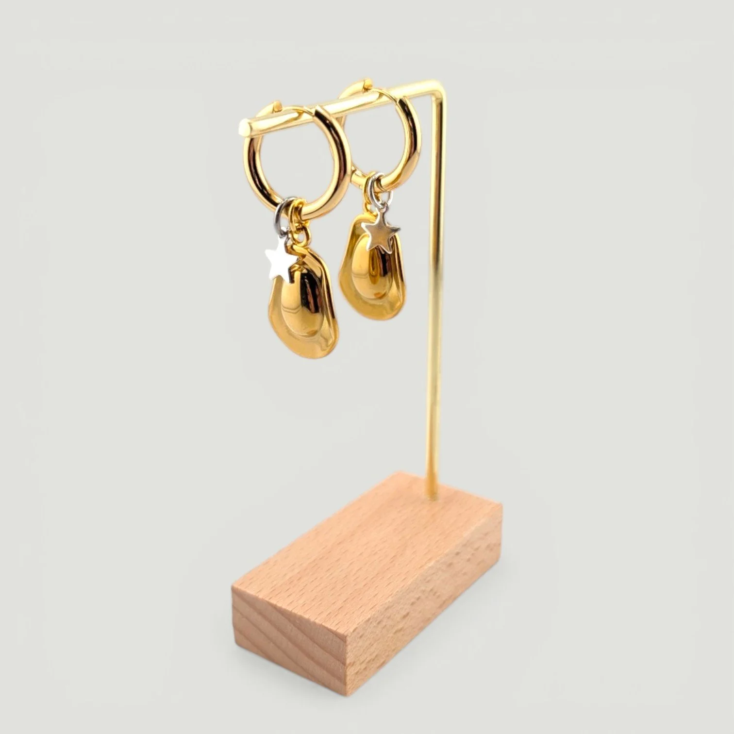 Gold cowboy hat and star charm huggie hoop earrings on display stand, showing drop and movement