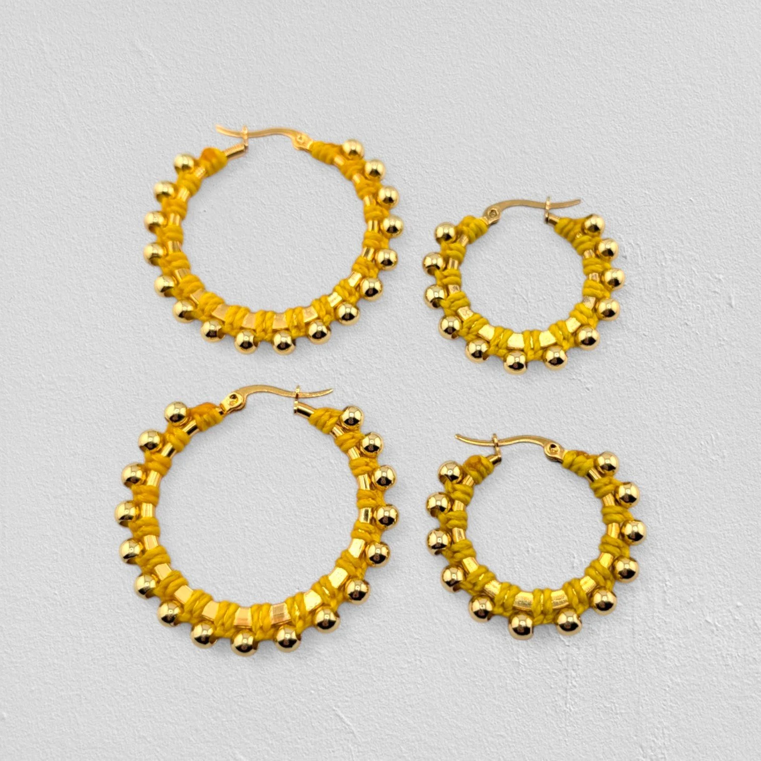 yellow beaded macramé stainless steel hoop earrings in gold, 30 mm and 40 mm sizes side by side, flat lay on a neutral background