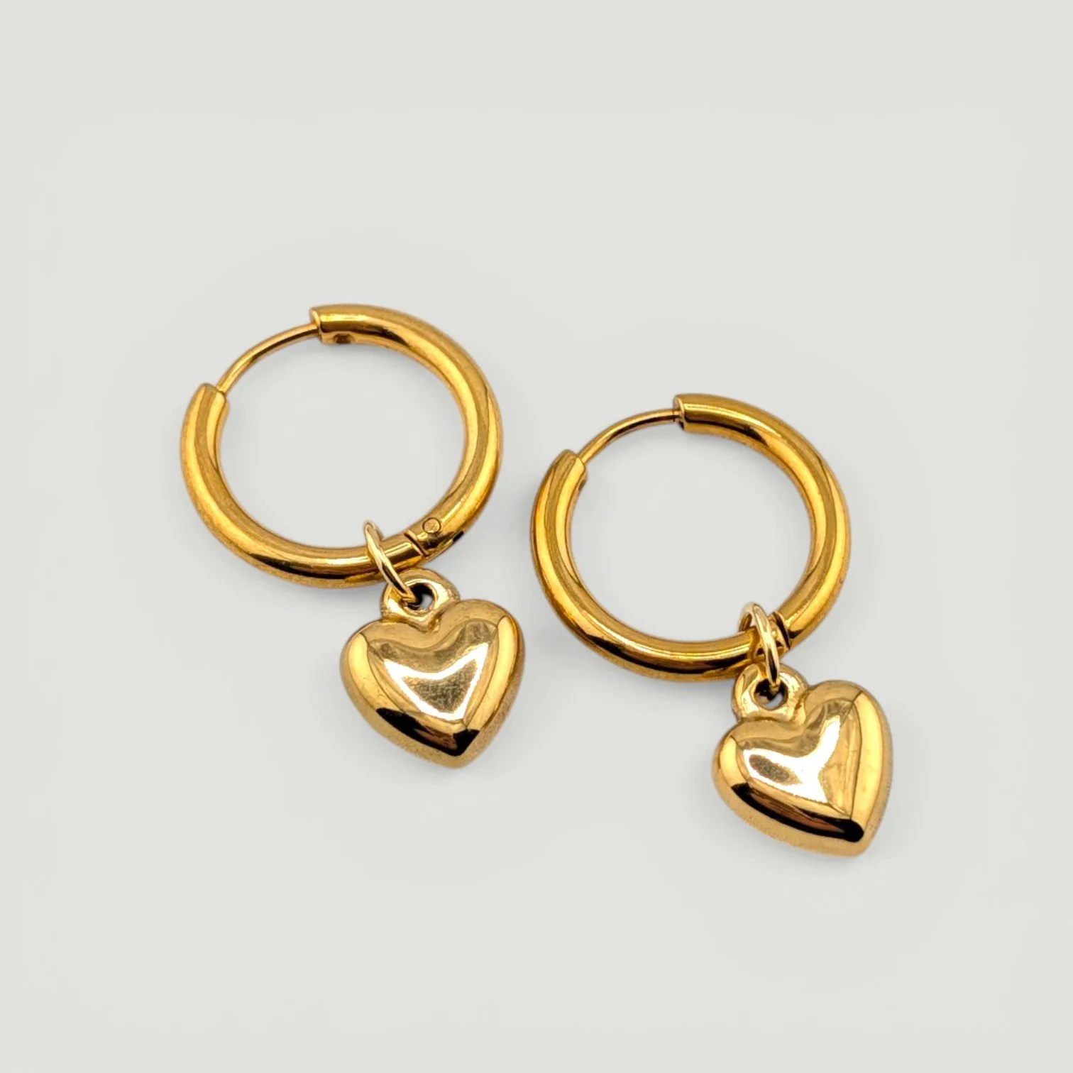 gold puffy heart huggie hoop earrings hanging on an earring stand, showing full shape and shine