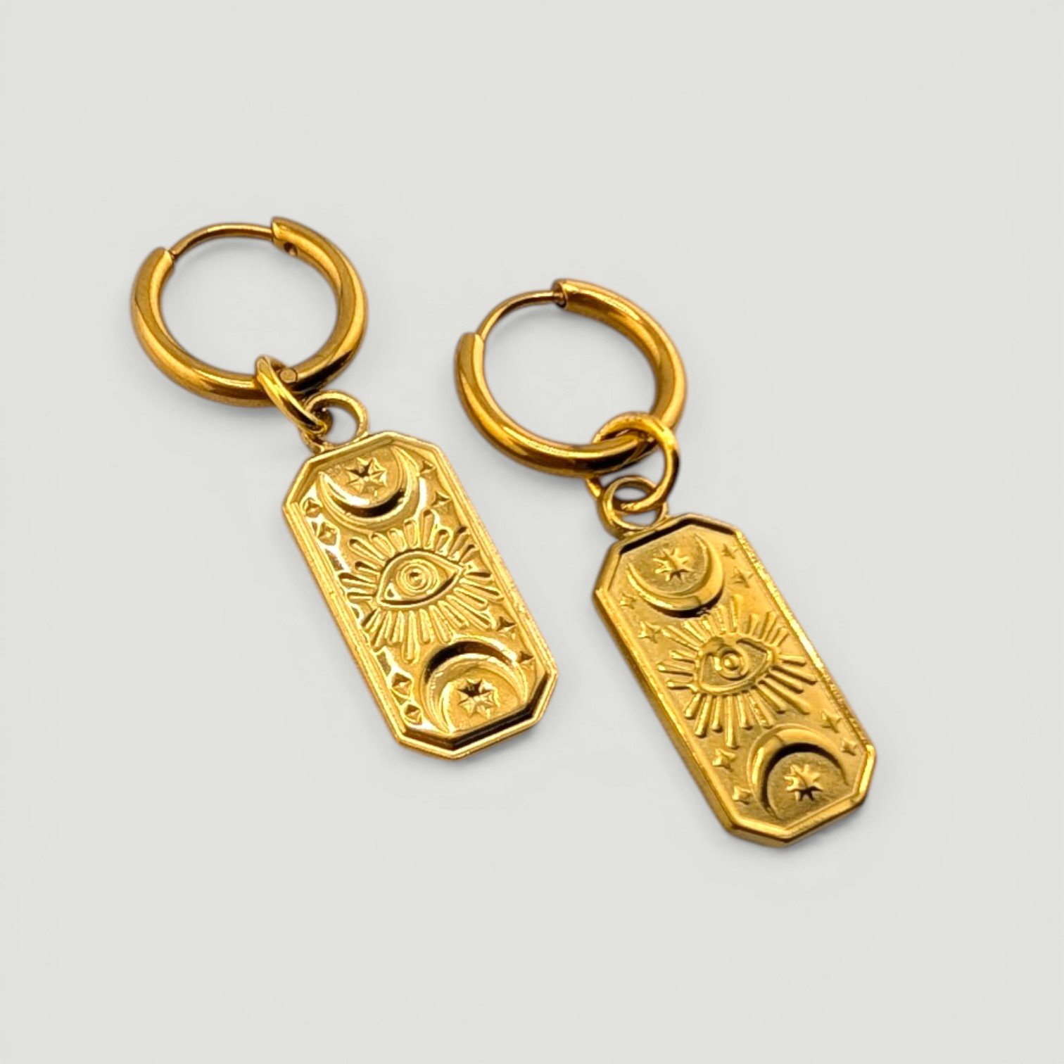 Gold stainless steel huggie hoop earrings with evil eye medallion charms flat lay