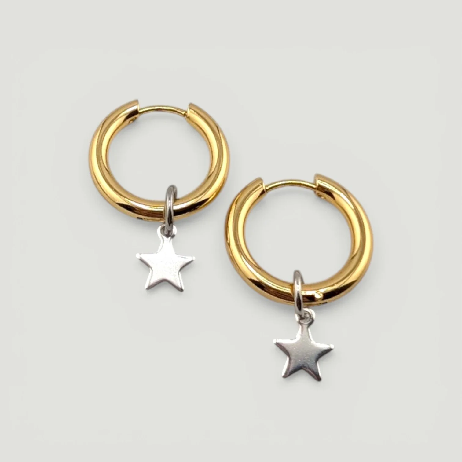 Gold stainless steel huggie hoop earrings with small star charm, flat lay
