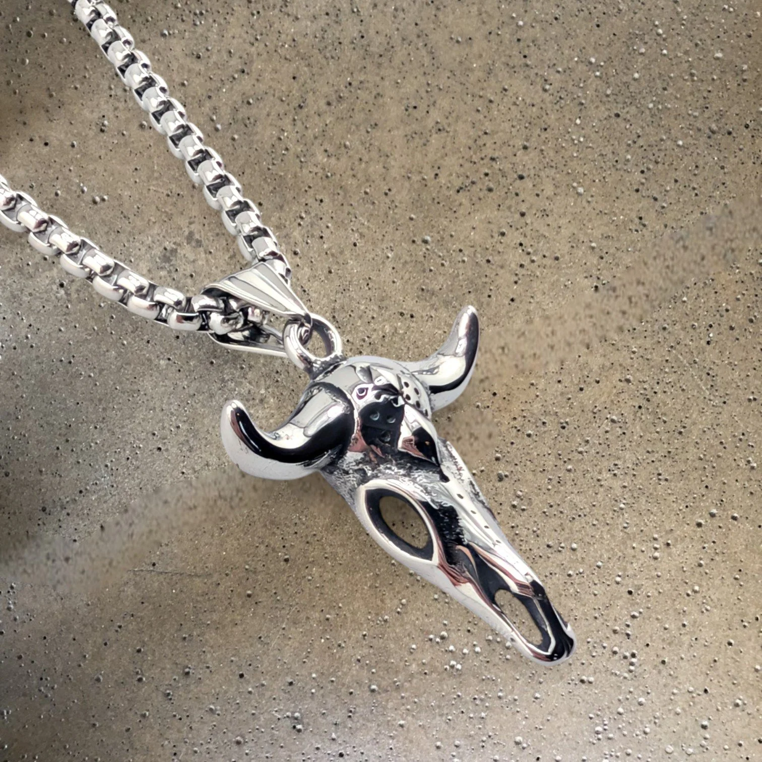 men's bull skull silver stainless steel necklace side view close up on textured background