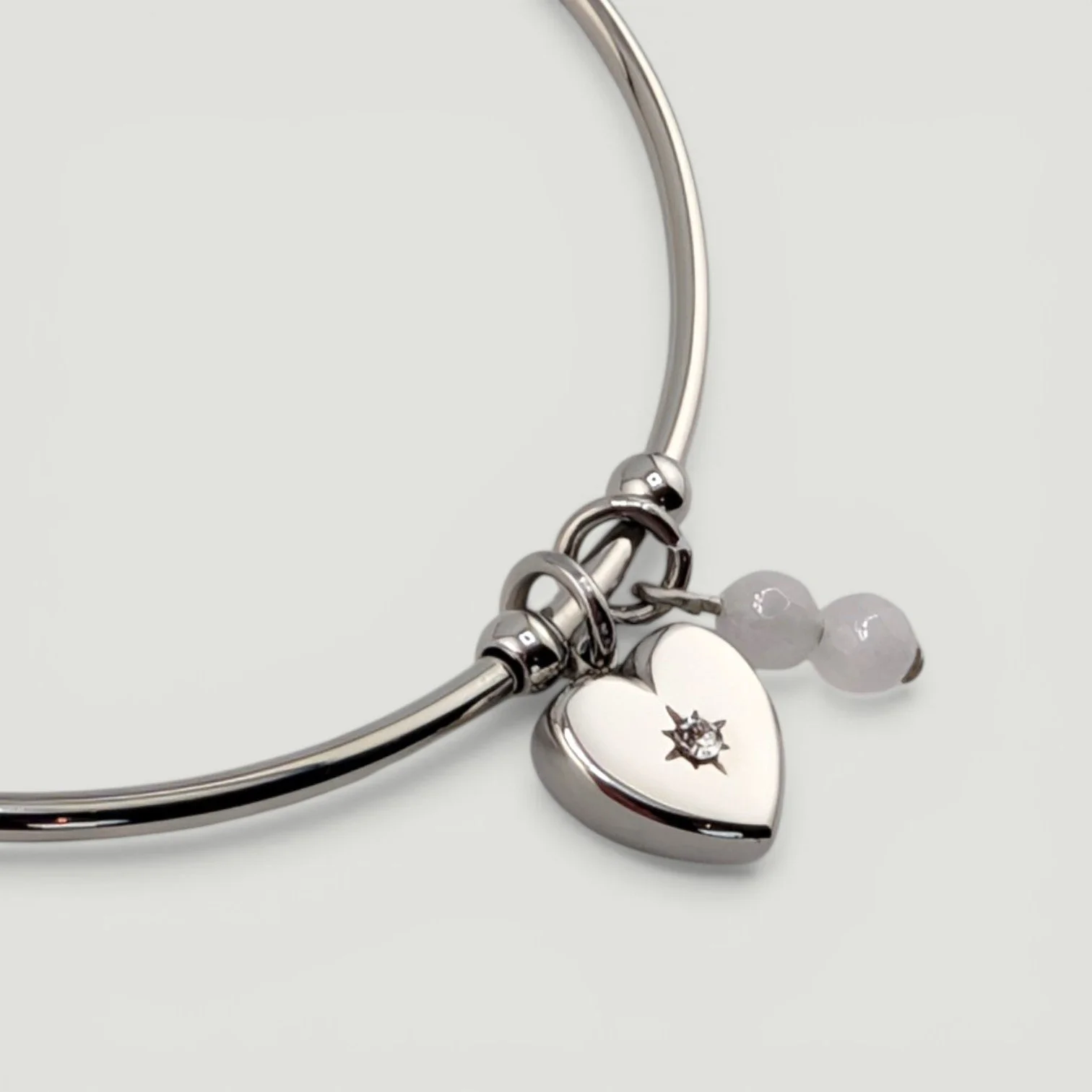 Silver starburst heart stainless steel bangle bracelet with rose quartz charm, close-up