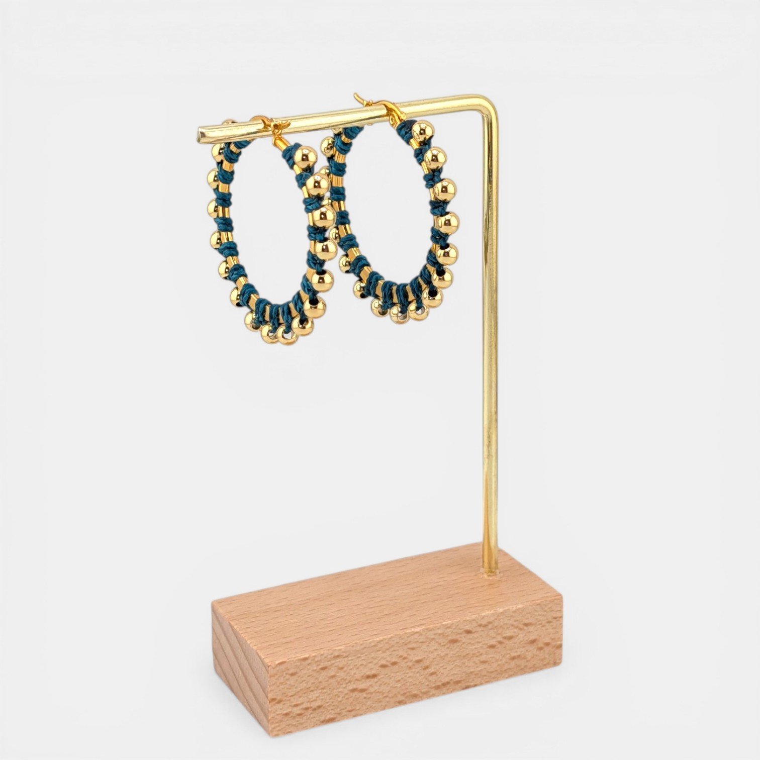 Teal beaded macramé stainless steel hoop earrings in gold, 40 mm drop shown on earring display stand