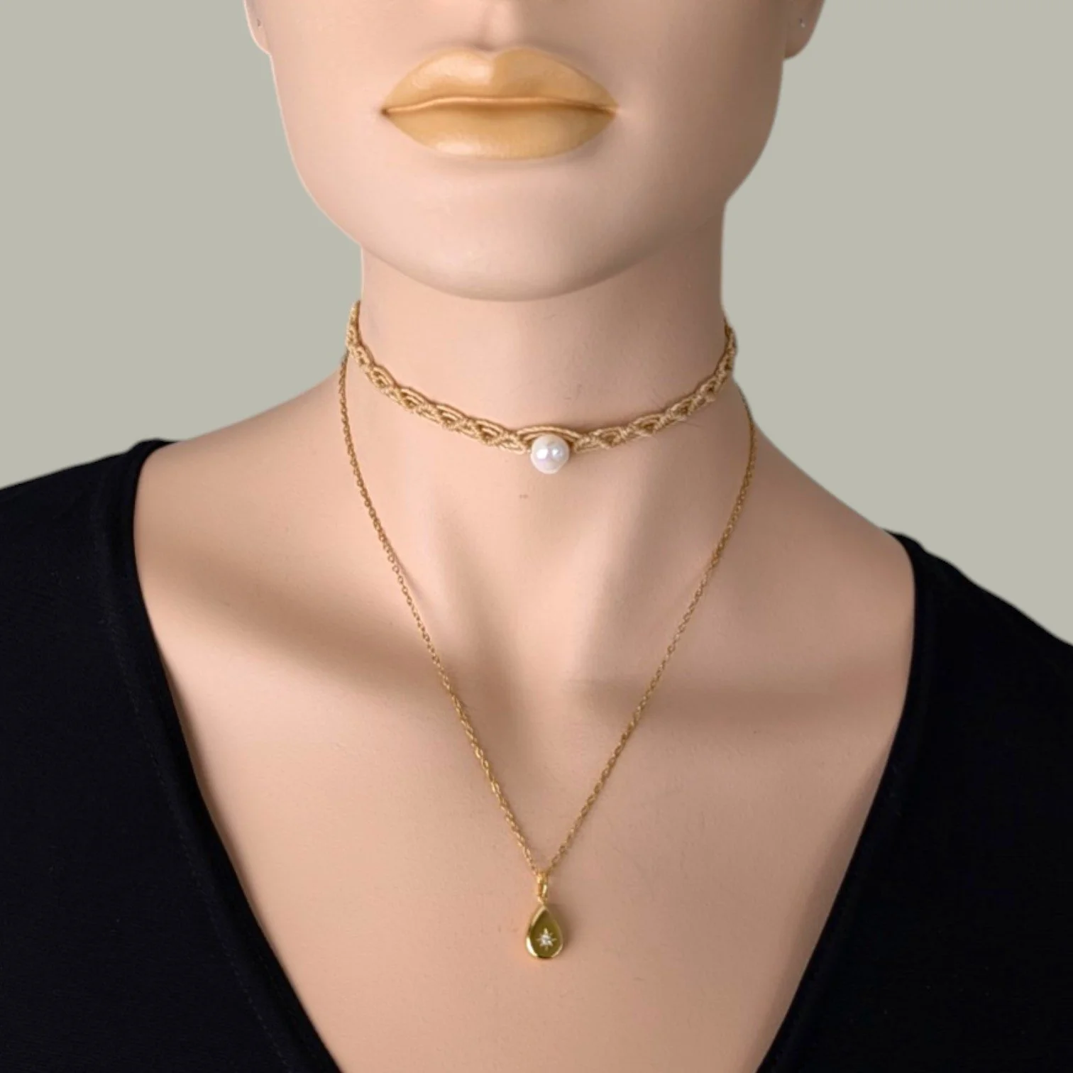 Gold stainless steel starburst teardrop necklace layered with macrame pearl choker on mannequin, close up bust view