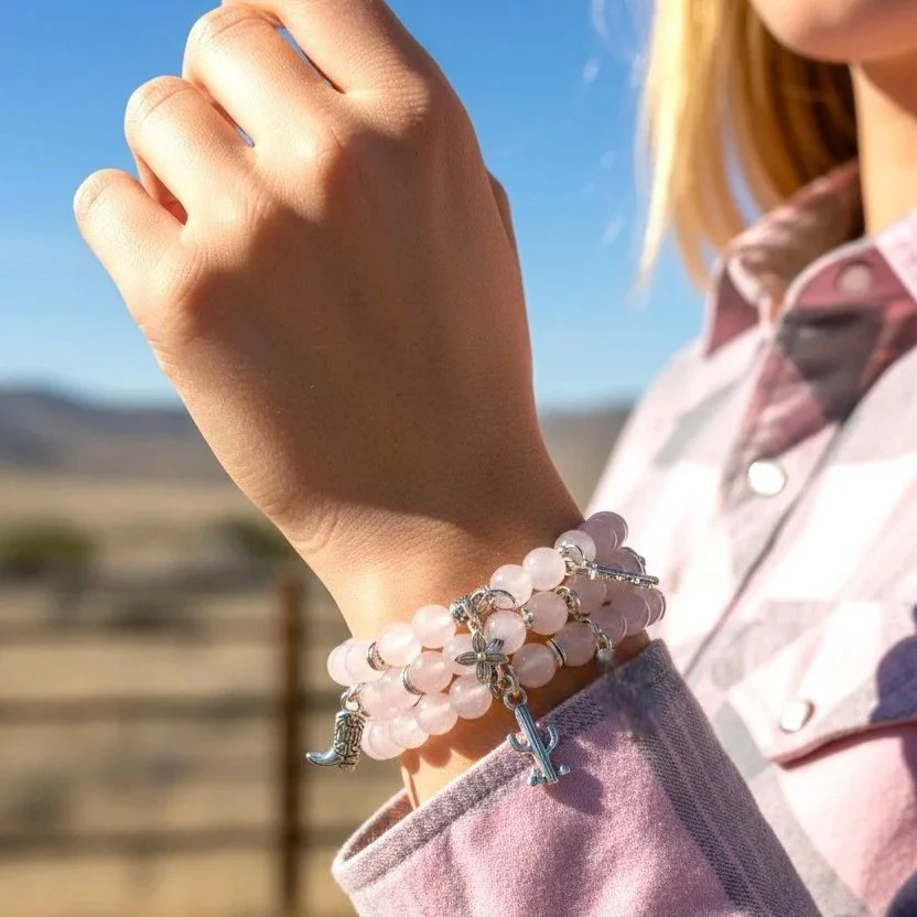 cowgirl in a country setting wearing a stack of rose quartz bracelets with western charms