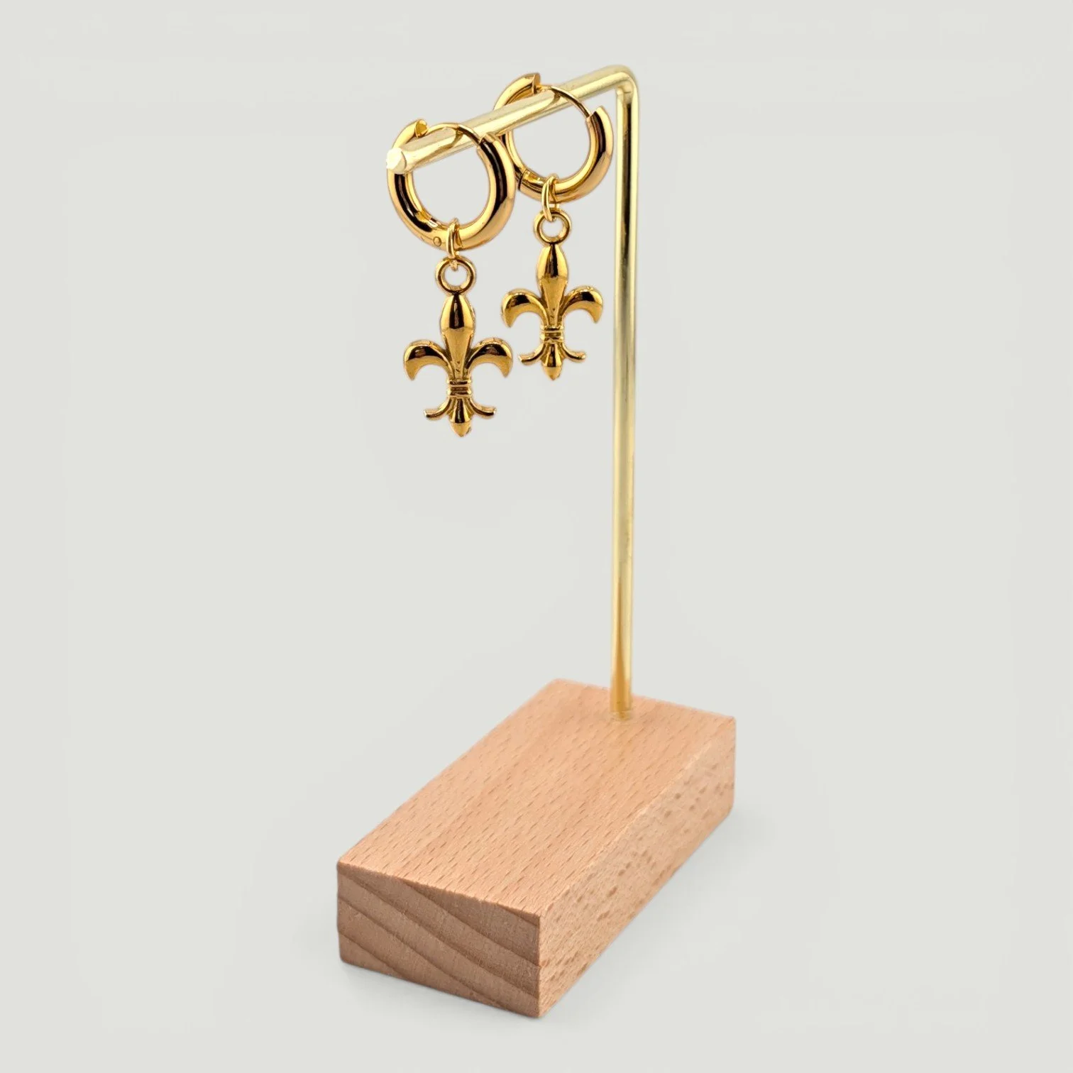 fleur de lis stainless steel huggie hoop earrings, gold, on earring stand, drop view