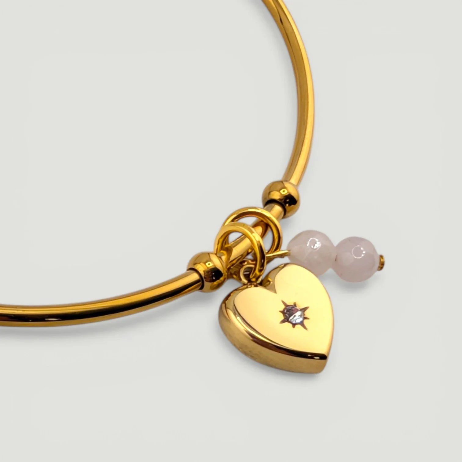 Gold starburst heart stainless steel bangle bracelet with rose quartz charm, close-up