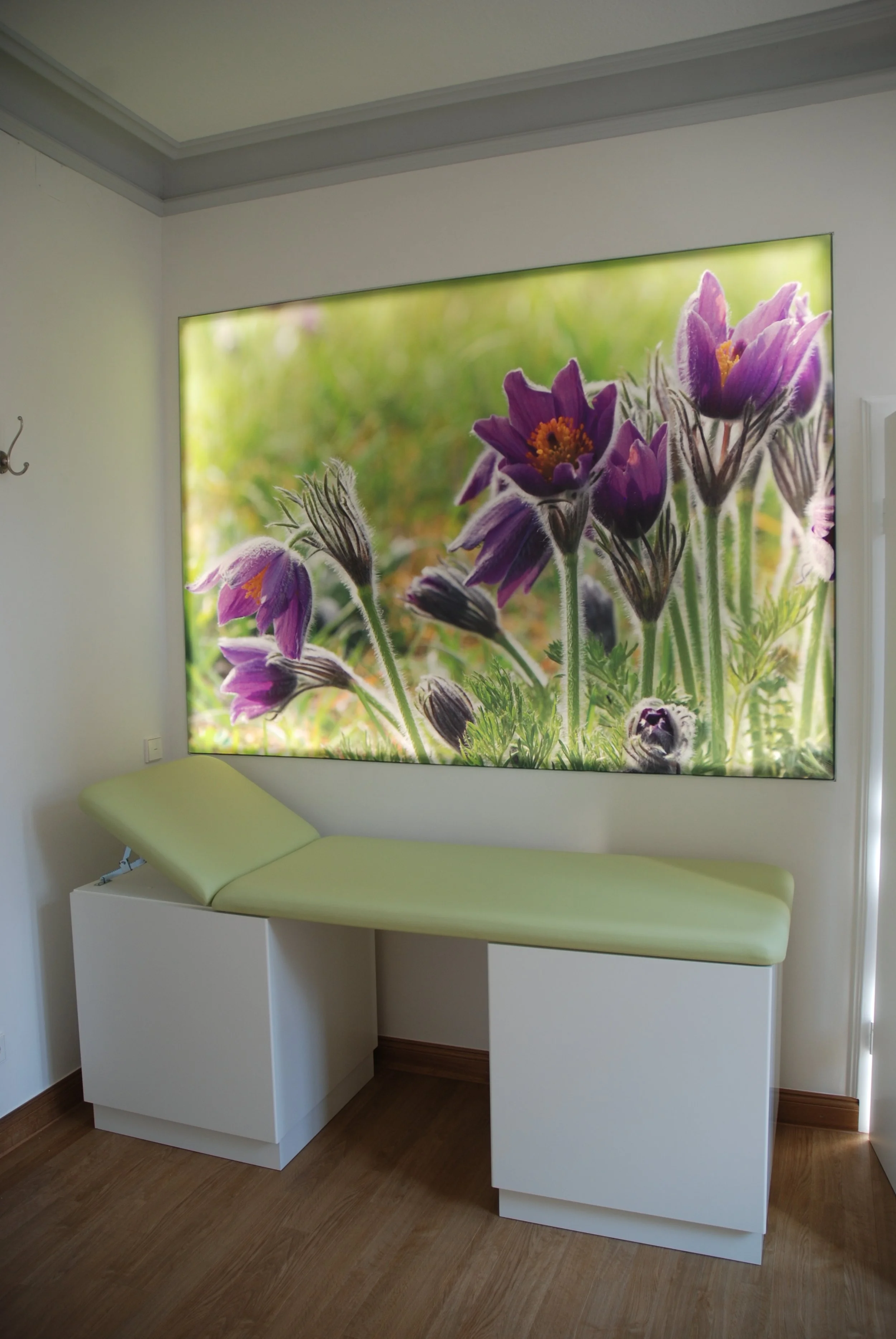Behandlungsbett in einem Behandlungsraum mit Wandbild von Lavendelblumen