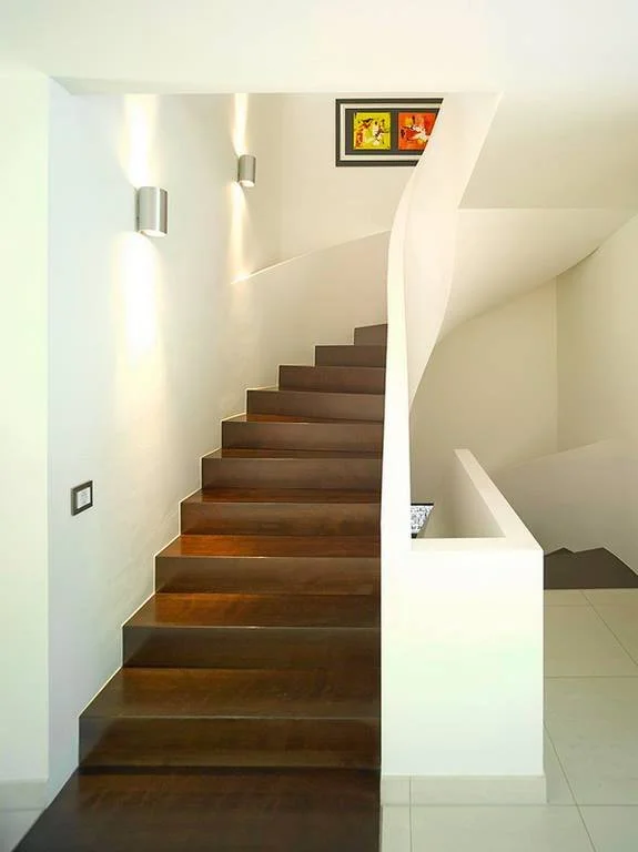 Holztreppe im modernen, hell erleuchteten Haus mit weißen Wänden und abstrahierter, bunter Kunst an der Wand.