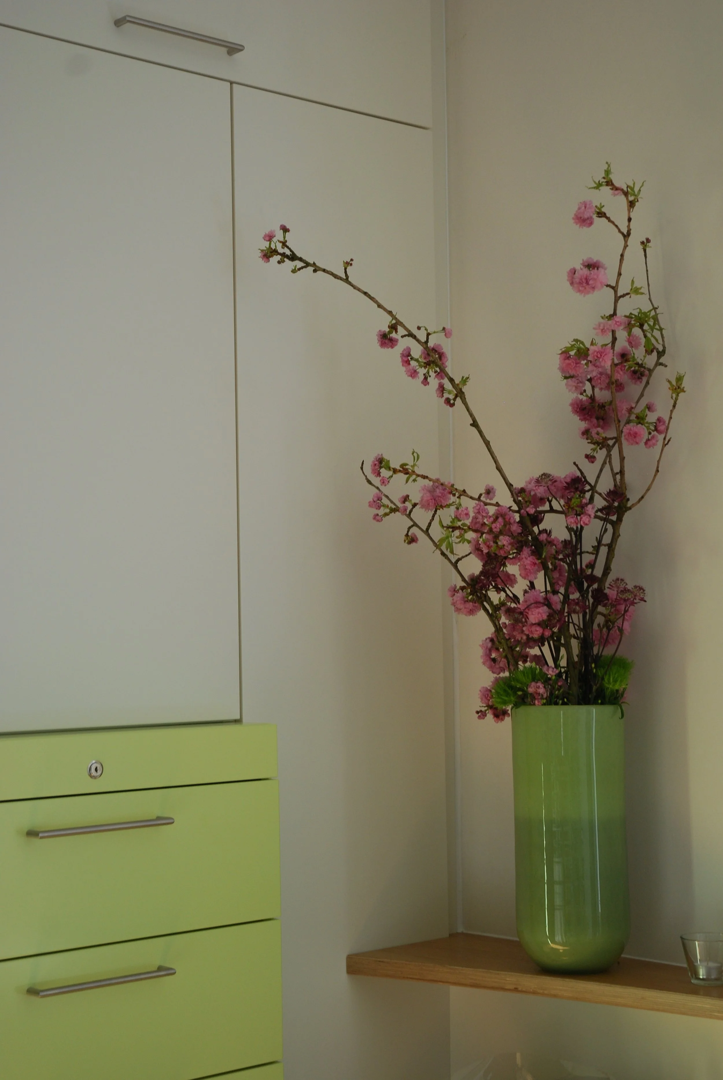 Vase mit pinken Zweigen und Blüten auf einer Holzablage in einer modernen Wohnung.