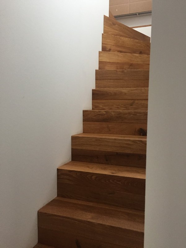 Holztreppe in einem Innenraum, seitenverkehrt mit weißen Wänden auf beiden Seiten.