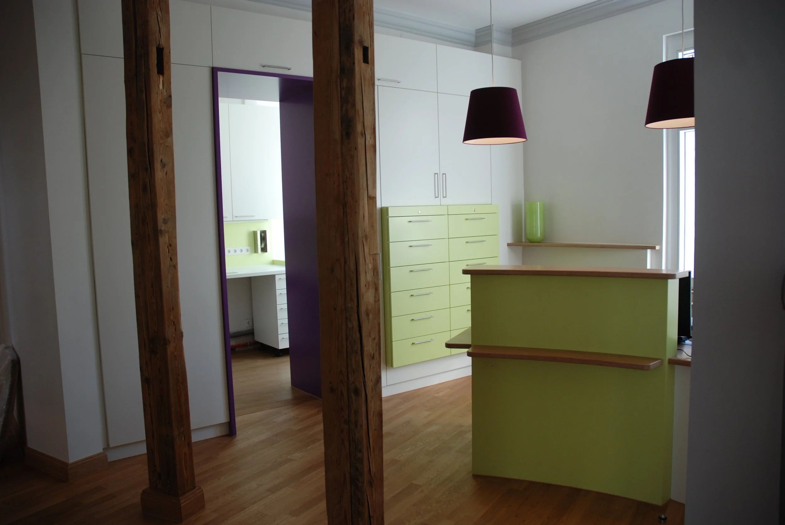 Innenraum einer modernen Wohnung mit Holzbalken, weißen Wänden, grünen Schränken, einer Theke und schwarzen Lampen. Es gibt einen Raum mit einer kleinen Barriere und offenen Blick auf den Flur.