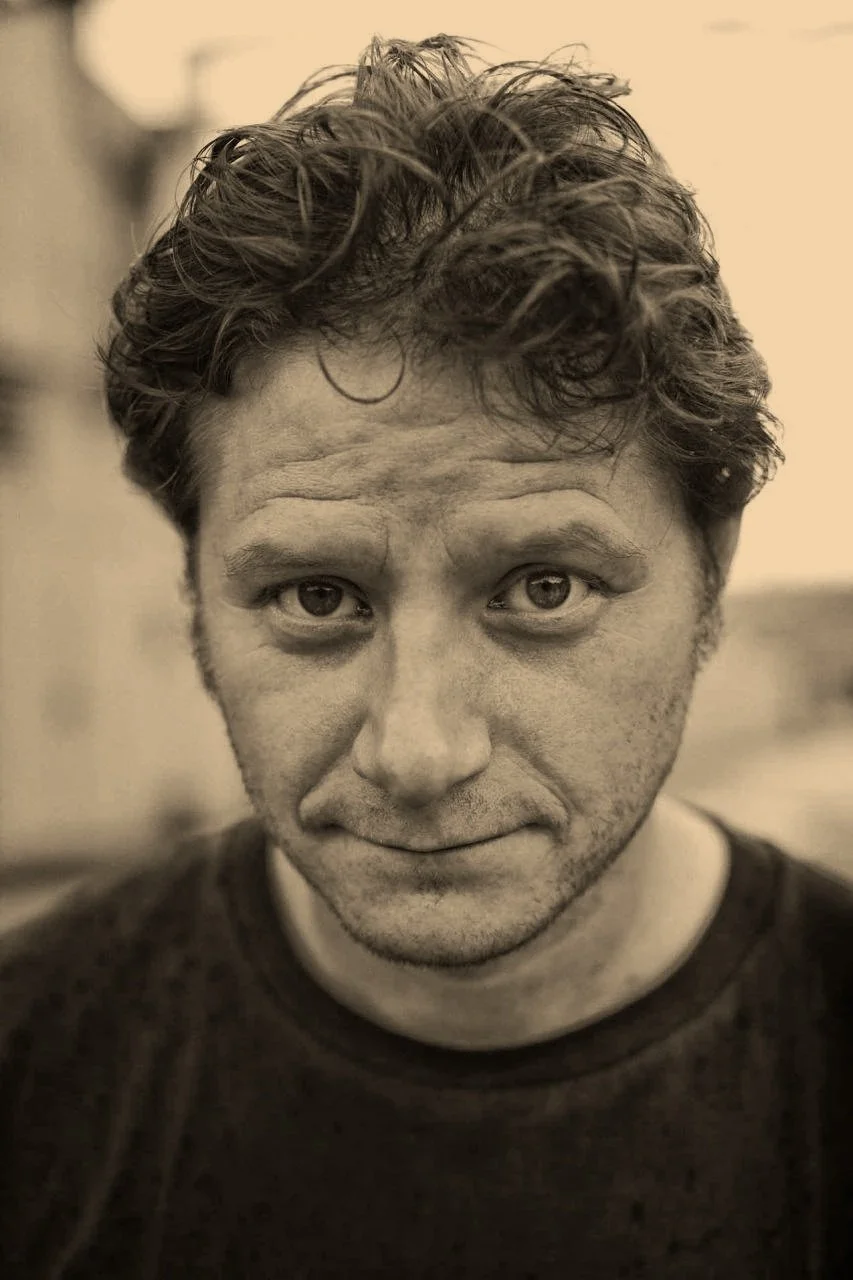 A black and white close-up portrait of a man with wavy hair looking directly at the camera.