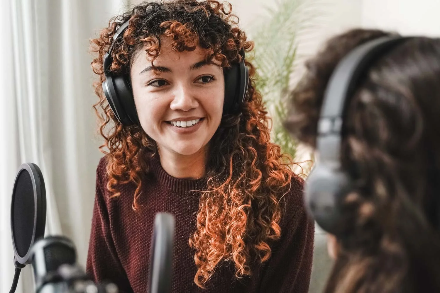Two women podcasting with headphones and microphones.