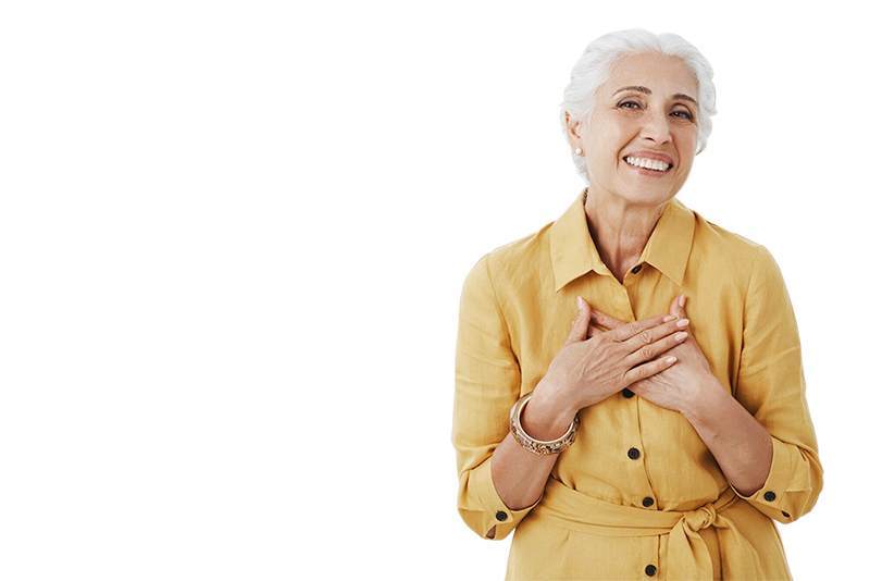 An elderly woman with gray hair smiling and holding her hands over her chest in a caring gesture.