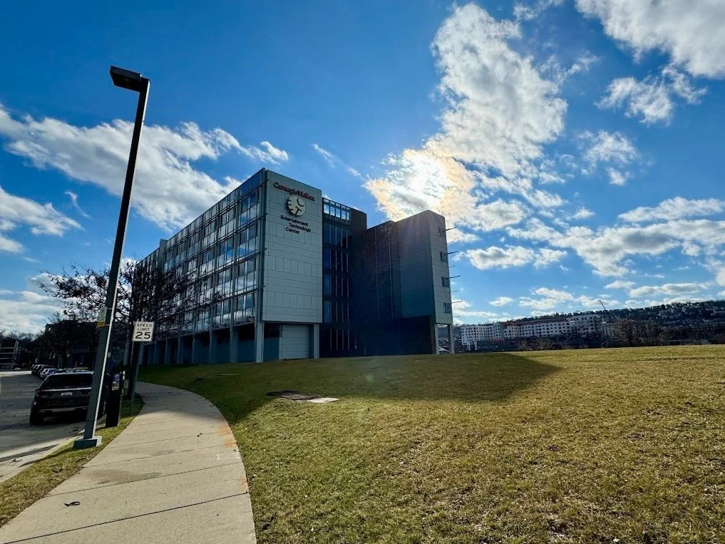 Exterior view of Carnegie Mellon University Entertainment Technology Center building under a partly cloudy sky, with a sidewalk, grass, and parked cars in the foreground.