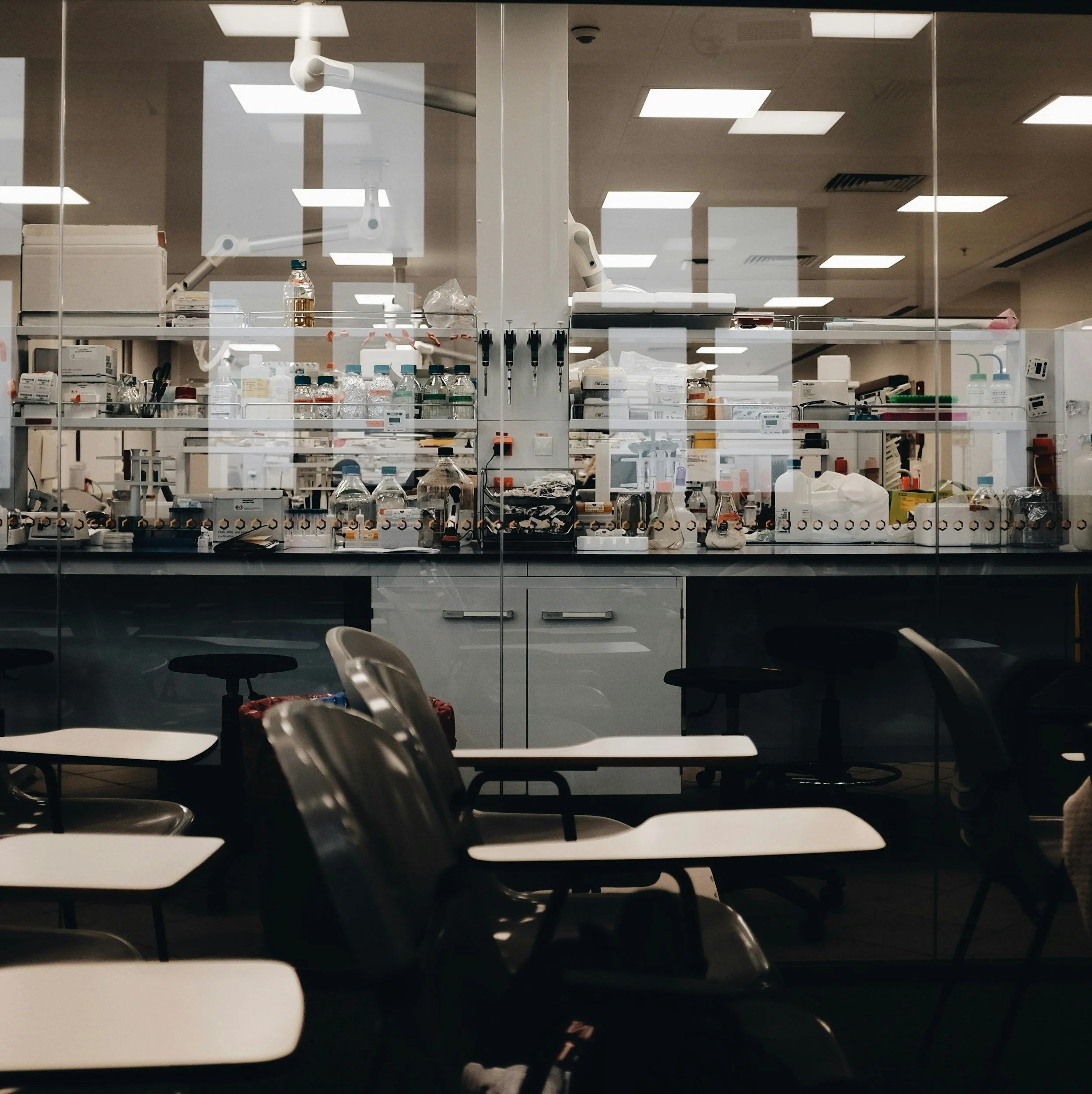 A view of a scientific laboratory seen through a glass window, with empty chairs and tables in the foreground.