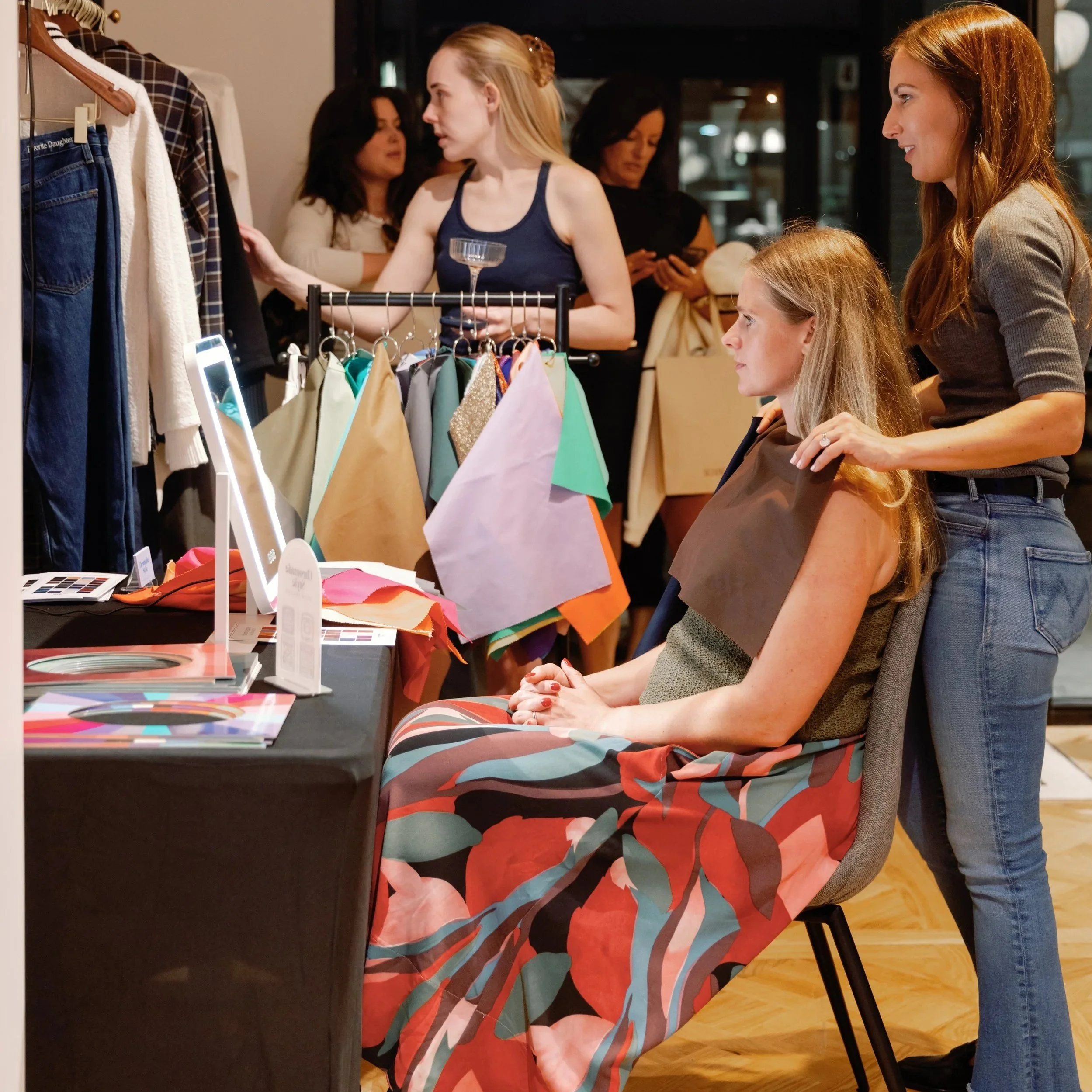 Women getting a color analysis session done for a brand activation and shopping in a boutique clothing store, looking at clothes on a rack and trying on different outfits.