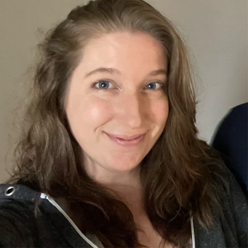 A woman with wavy brown hair and blue eyes smiling at the camera.