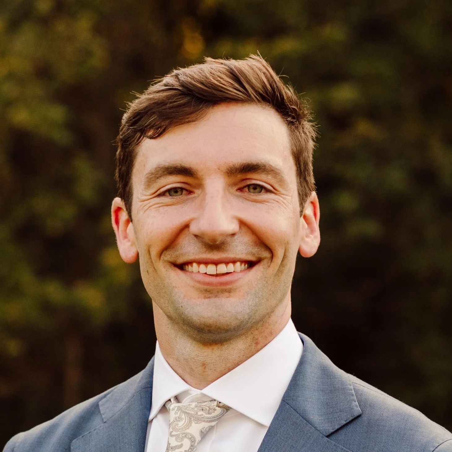 Jake Higdon - the founding director - wearing safety glasses, a yellow hard hat, and an orange safety jacket, speaking or explaining something with a control room or operations center with multiple monitors and control panels in the background.