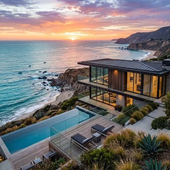Luxury modern house with glass balcony and swimming pool overlooking an ocean at sunset with rugged coastline.