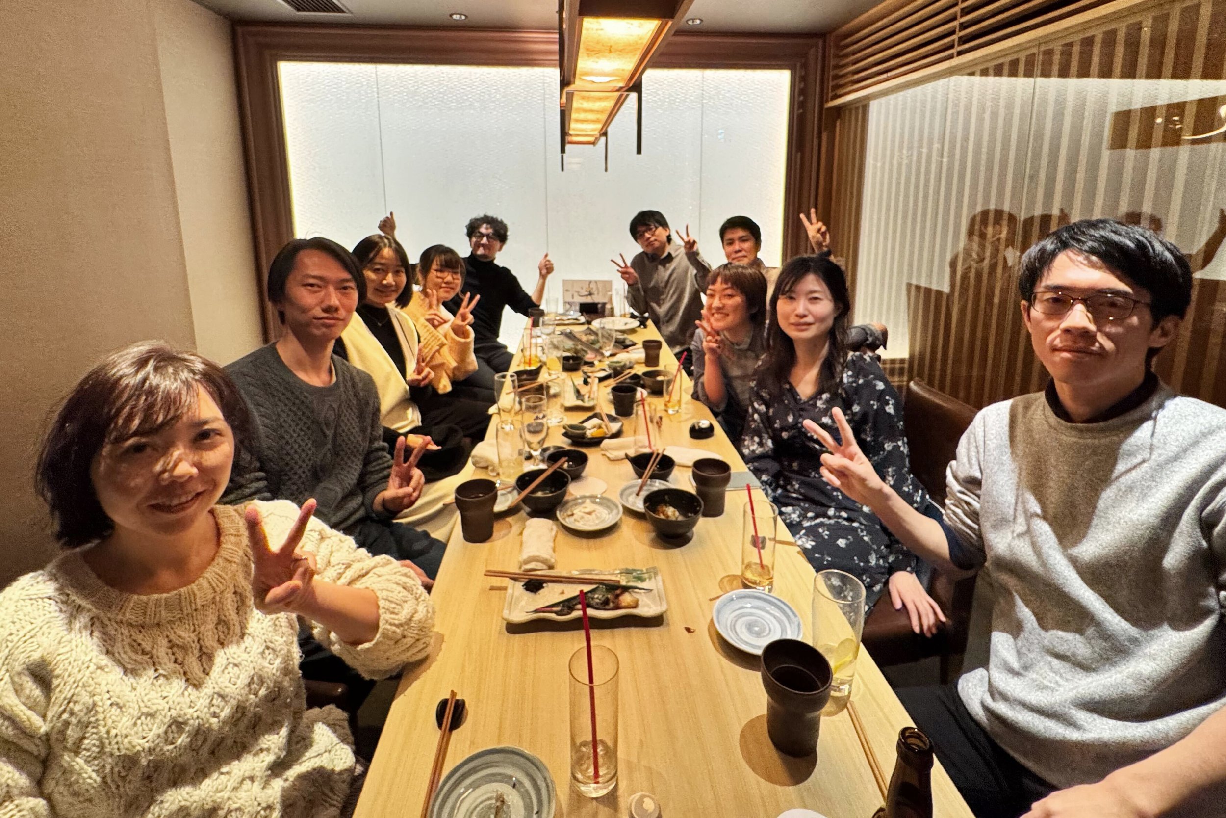 和食レストランでのグループの食事会の様子。テーブルに料理と飲み物が並び、参加者たちが笑顔でポーズをとっている。