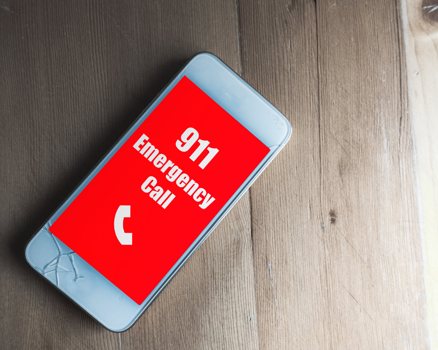 smart phone laying on a wood background displaying 911 Emergency Call against a red screen