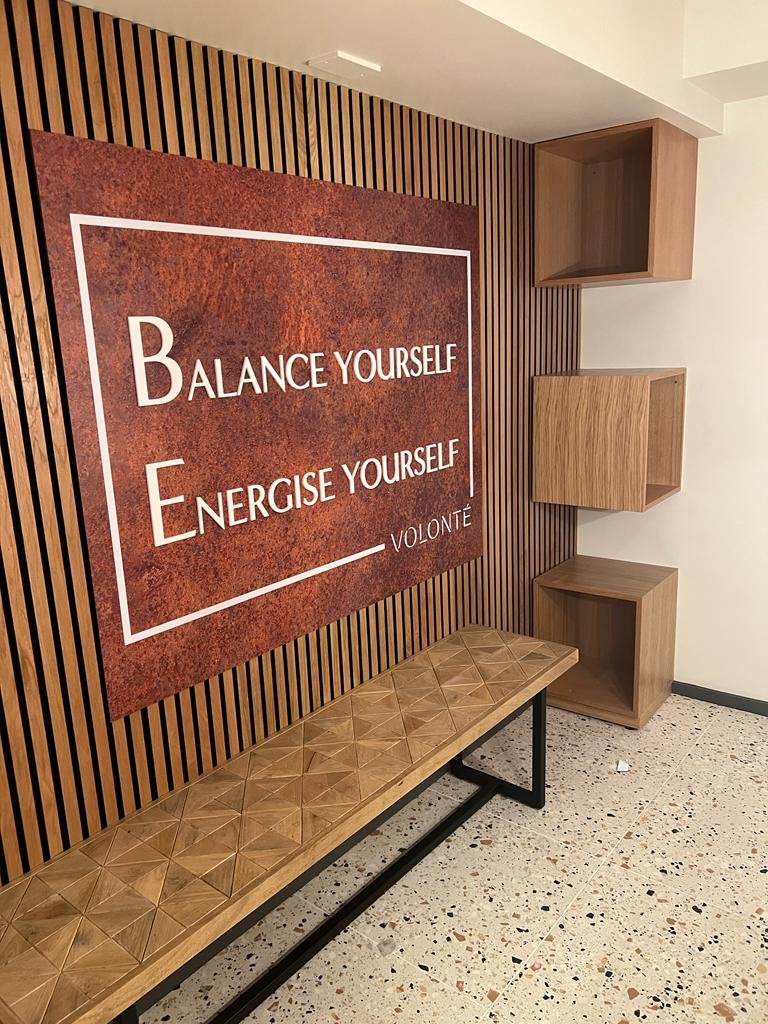Interior space with a wooden slat wall featuring a large red and white motivational quote, a wooden bench with a patterned surface, and three wooden cube shelves arranged vertically on the right side.
