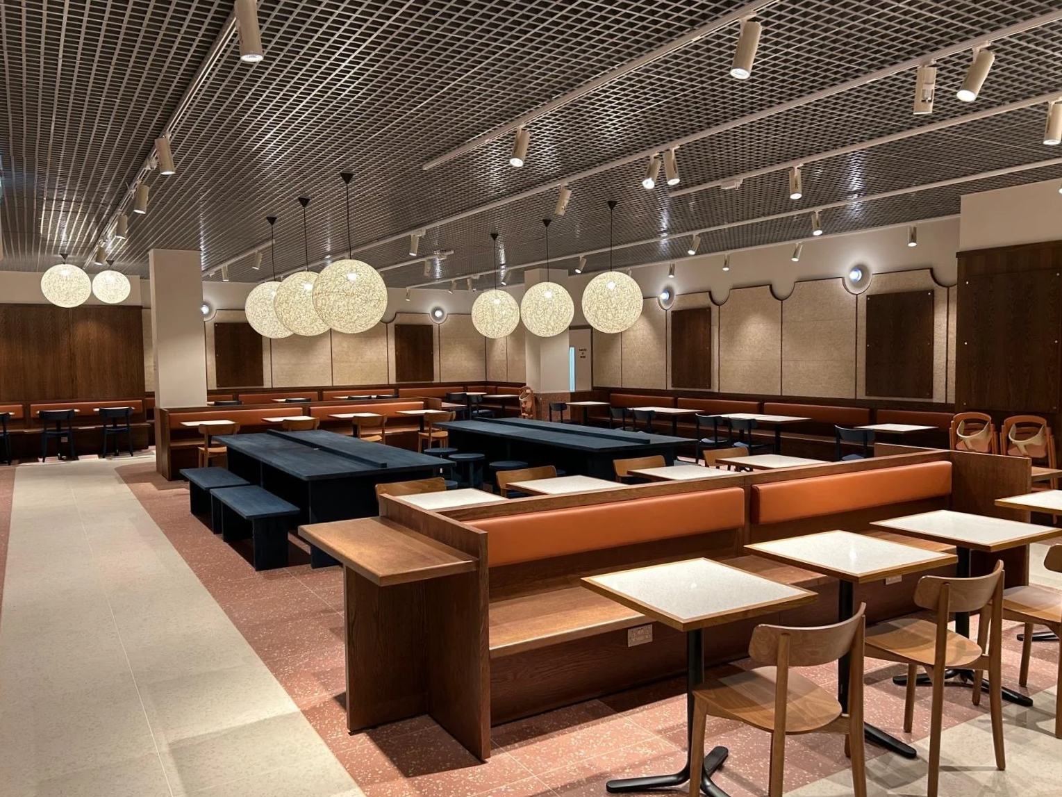 Empty restaurant with tables, chairs, hanging spherical light fixtures, and wooden wall panels.