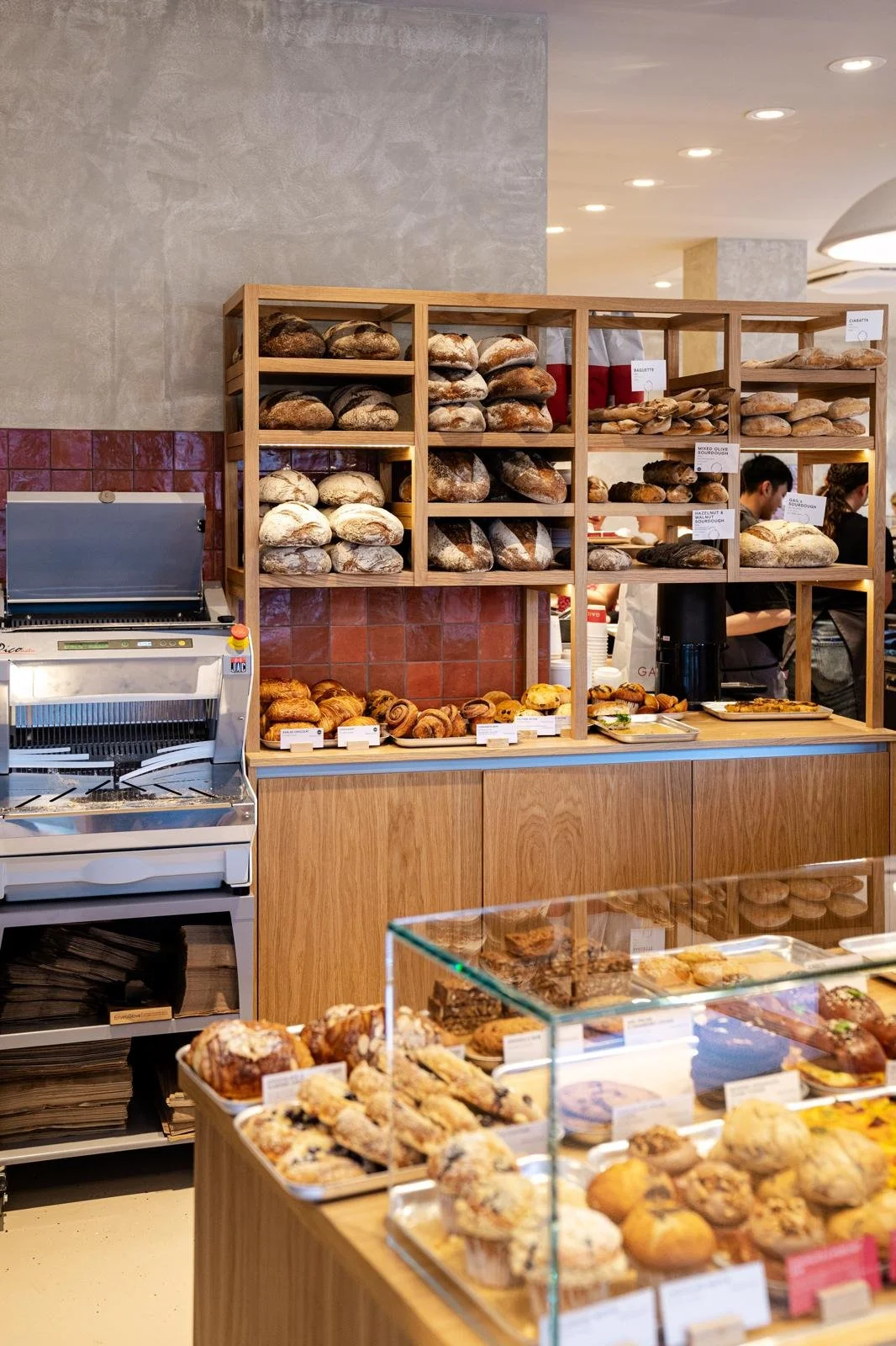 Display of assorted bread and baked goods in a bakery, including baguettes, croissants, muffins, and cookies.