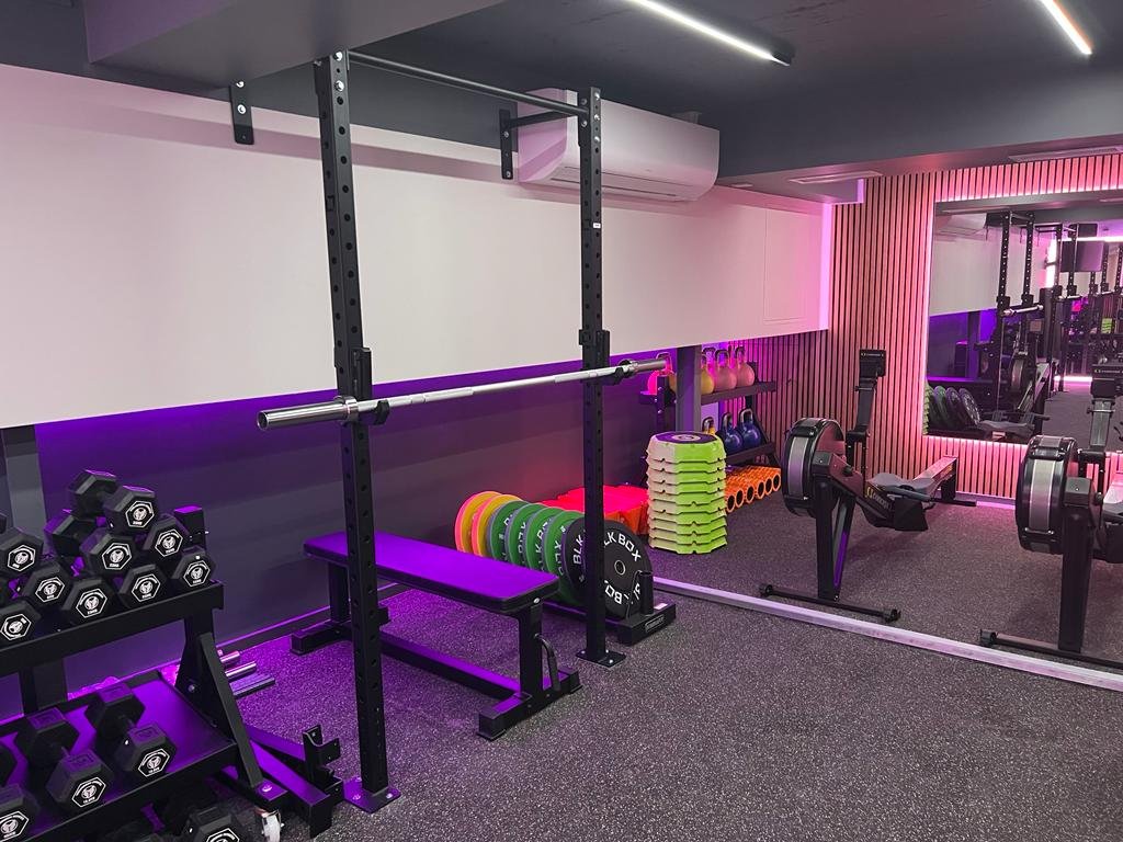 Interior view of a modern gym with weightlifting equipment, colored weights, and stationary bikes.
