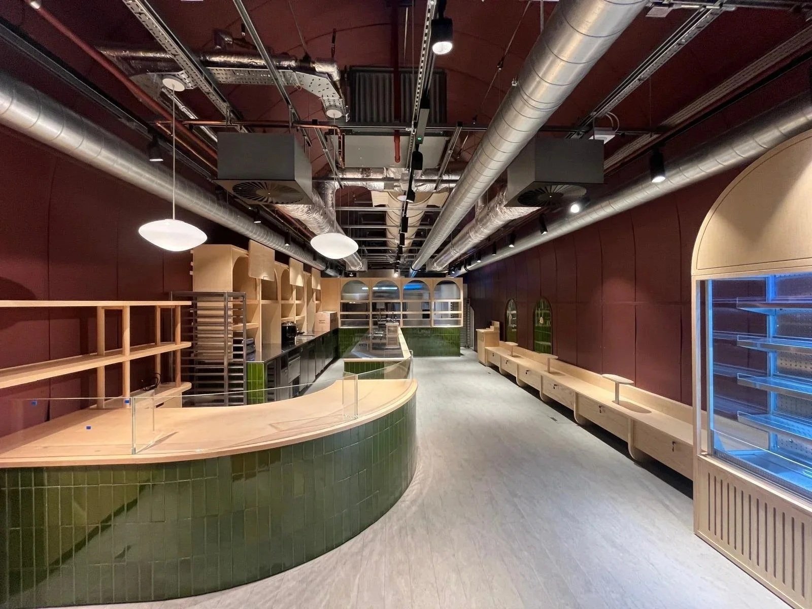 Empty counter and shelving inside a commercial space with pipes and ducts on the ceiling.