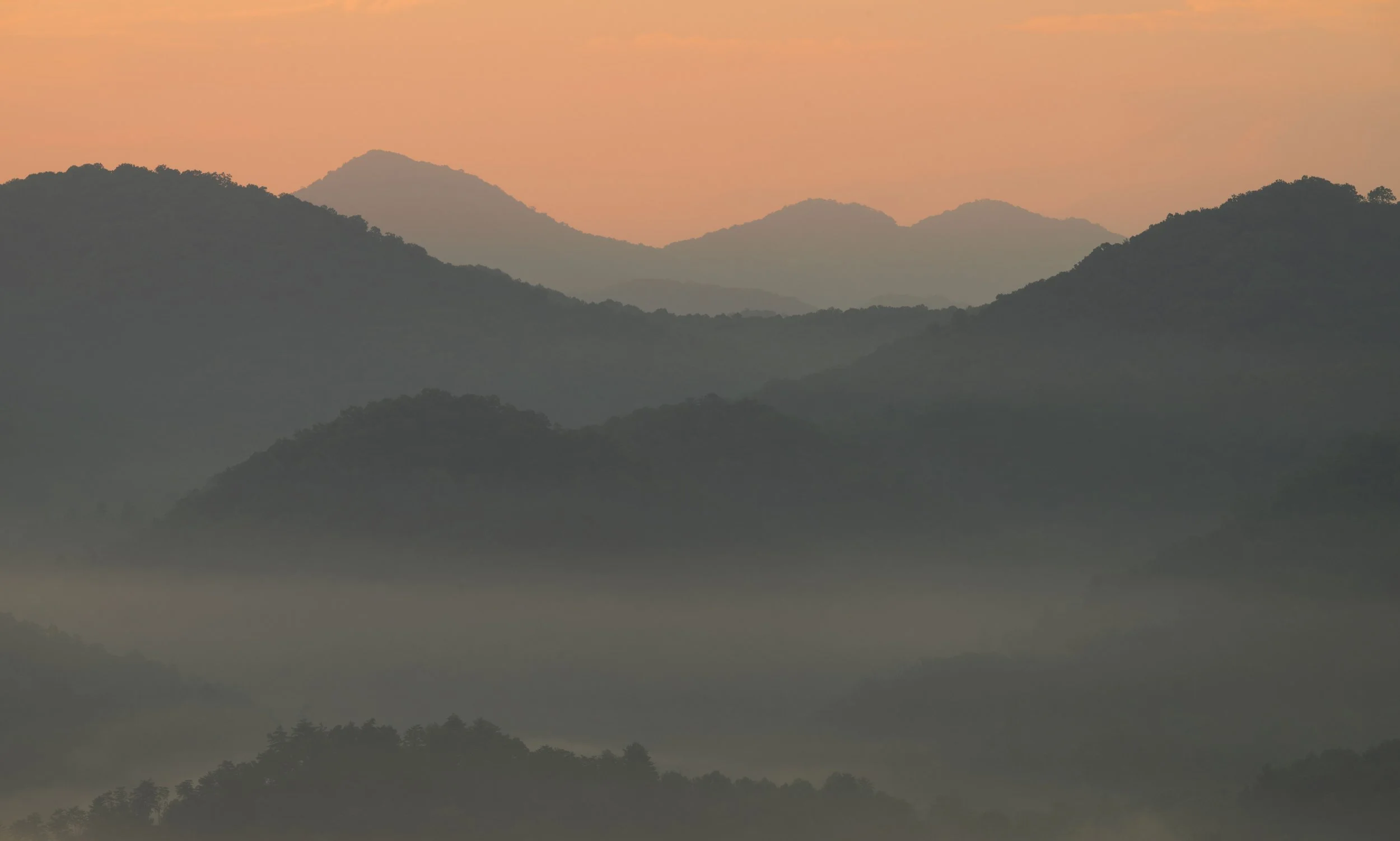 Sunset over misty mountain range with layered silhouettes.