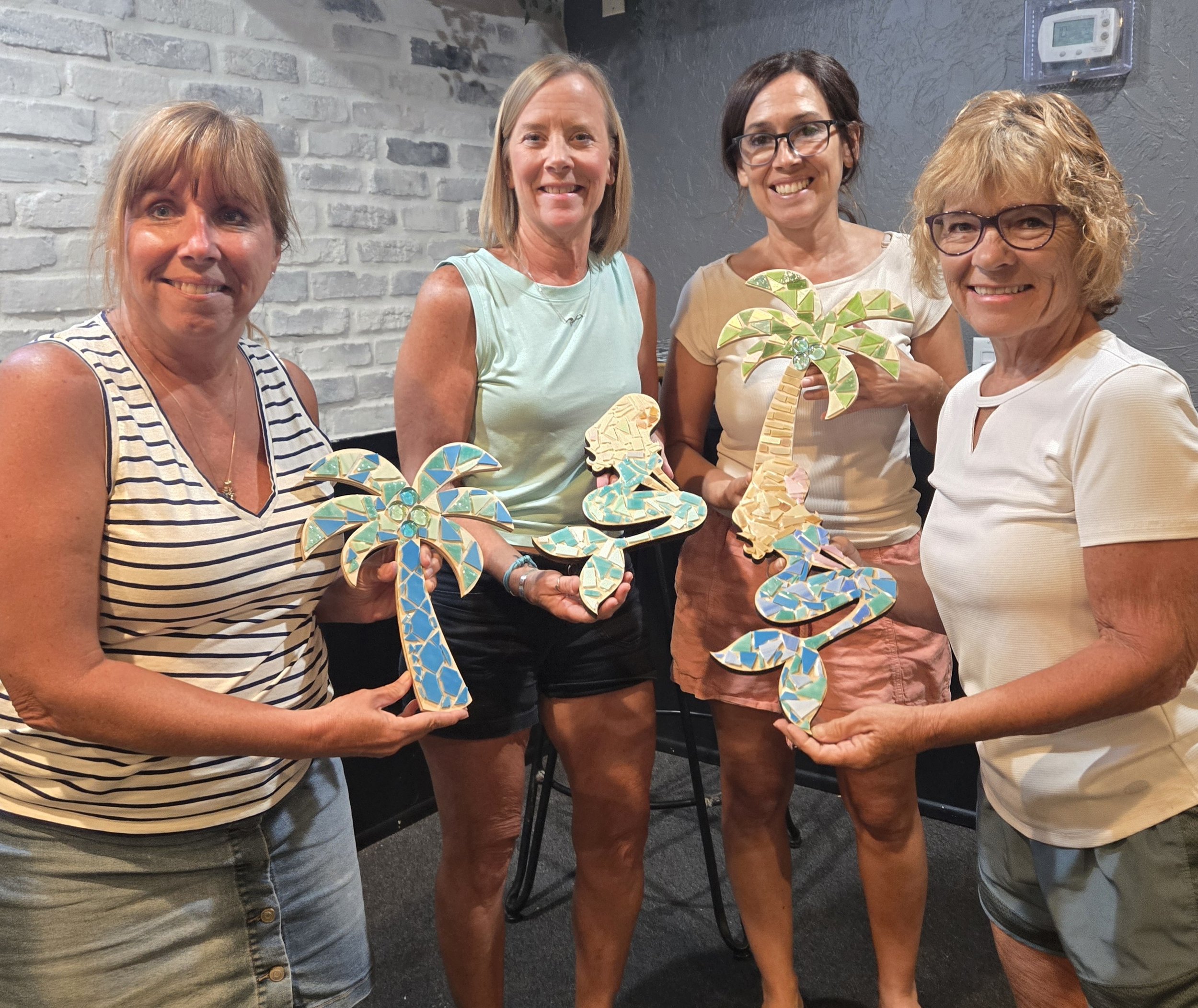Four women standing indoors holding mosaic-style palm tree and flower decor.