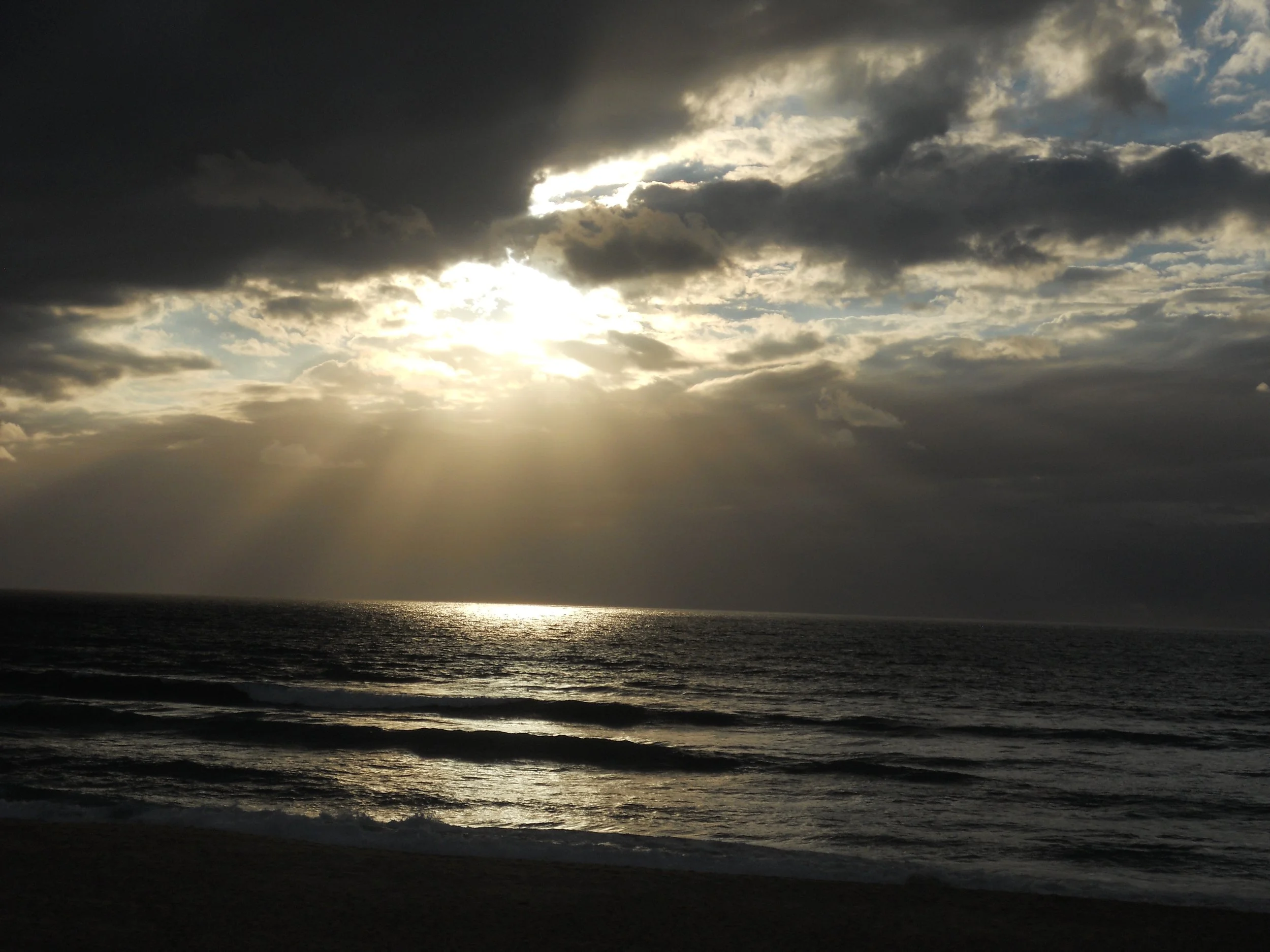 Ciel nuageux avec le soleil partiellement caché par des nuages lumineux au-dessus de la mer.