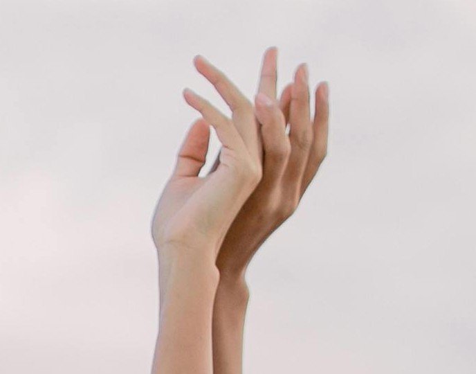 Two hands, one light-skinned and one dark-skinned, touching and overlapping against a plain background.