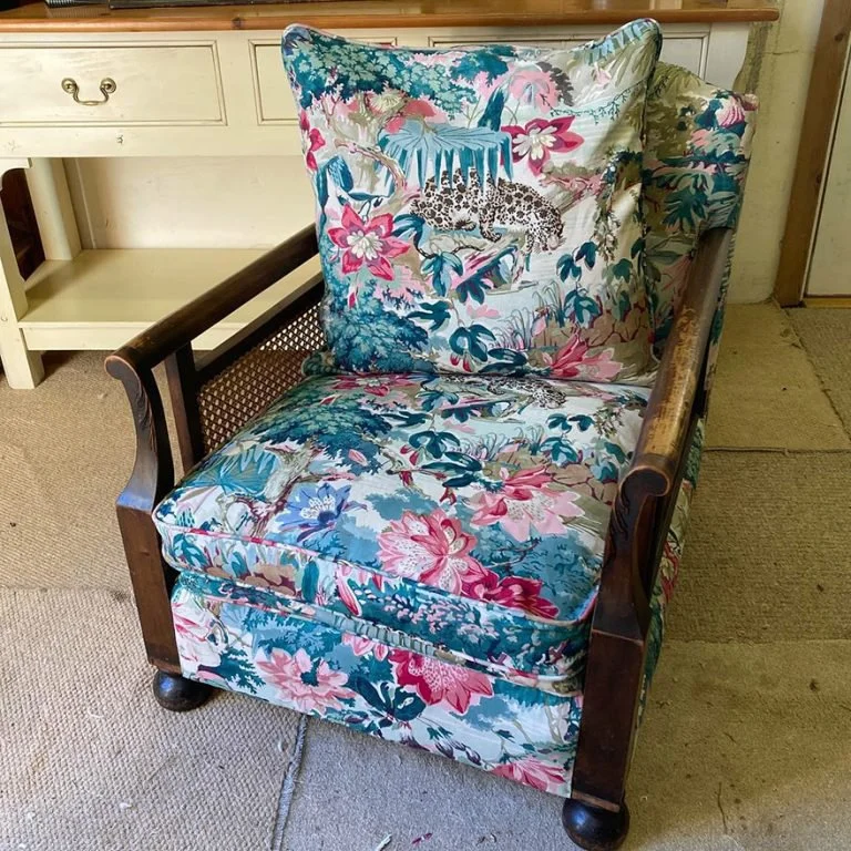 Antique Bergere armchair with cane sides reupholstered in Linwood Jungle Rumble Parrot linen fabric. As well as replacing all the old upholstery a new feather pad was constructed for the rear cushion along with new back and seat loose cushions.