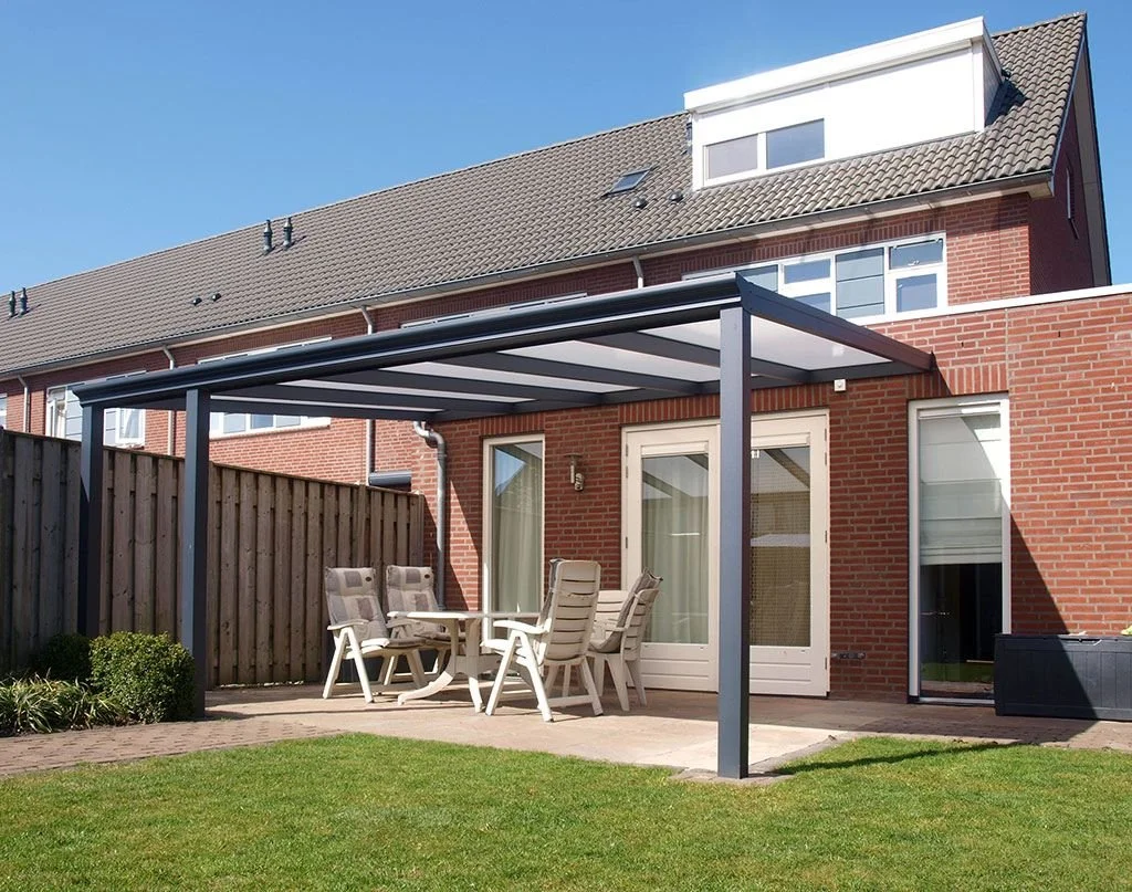Backyard patio area with a covered outdoor dining table and chairs, brick house with a sliding glass door, wooden privacy fence, and a blue sky.